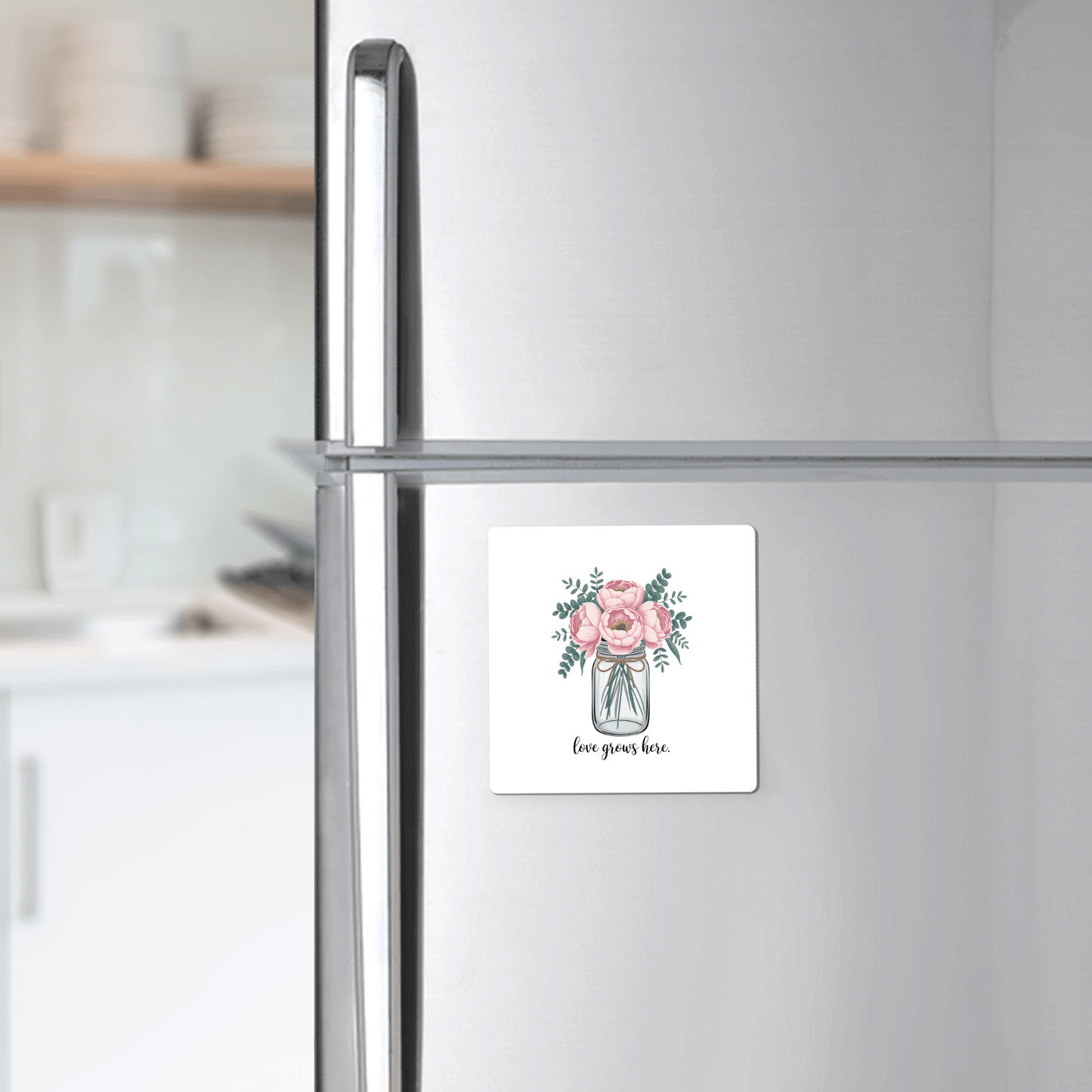The Love Grows Here Floral Magnet by Mirabilia Boutique, featuring pink flowers in a vase and "love grows here" script, brings charming farmhouse decor to any silver refrigerator in your kitchen.