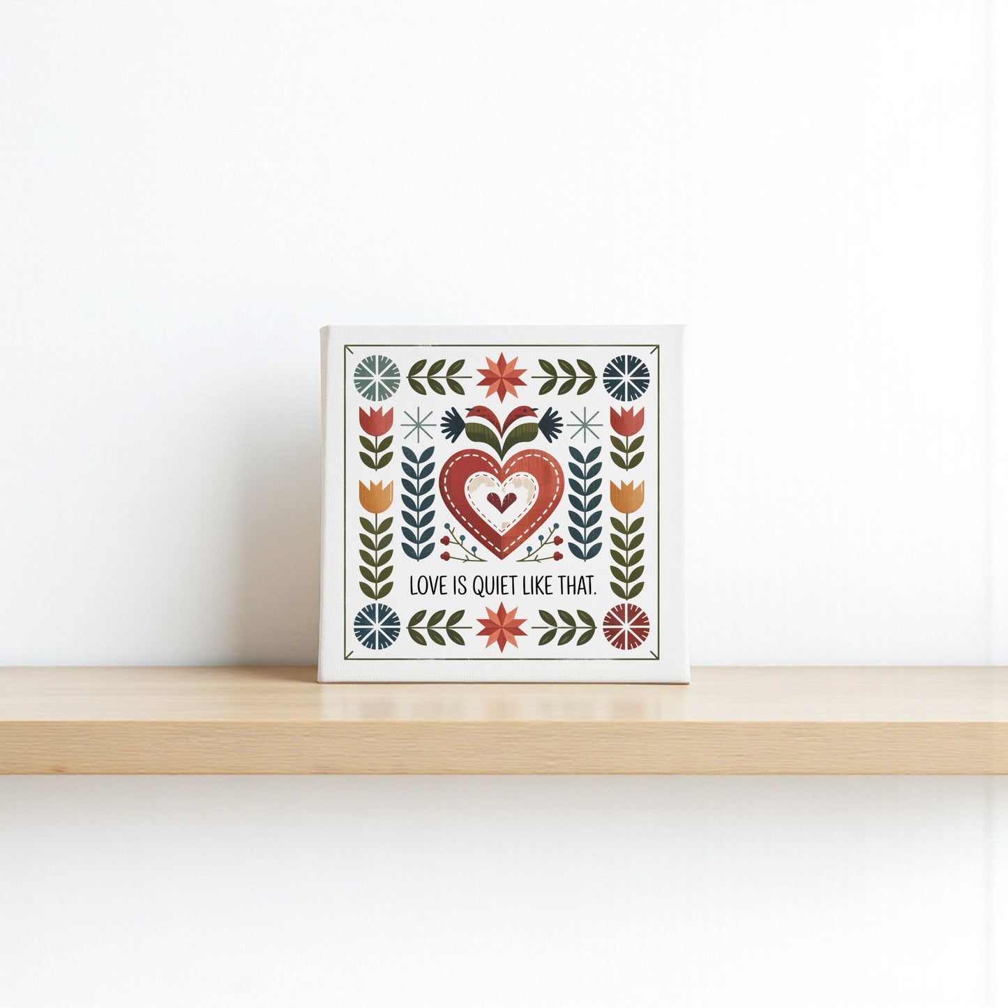 The Mirabilia Boutique "Love Is Quiet Like That Canvas" features a folk art heart and floral design on a white background, perfect for adding charm to your cozy decor. Ideal as a wall decor gift for any home.