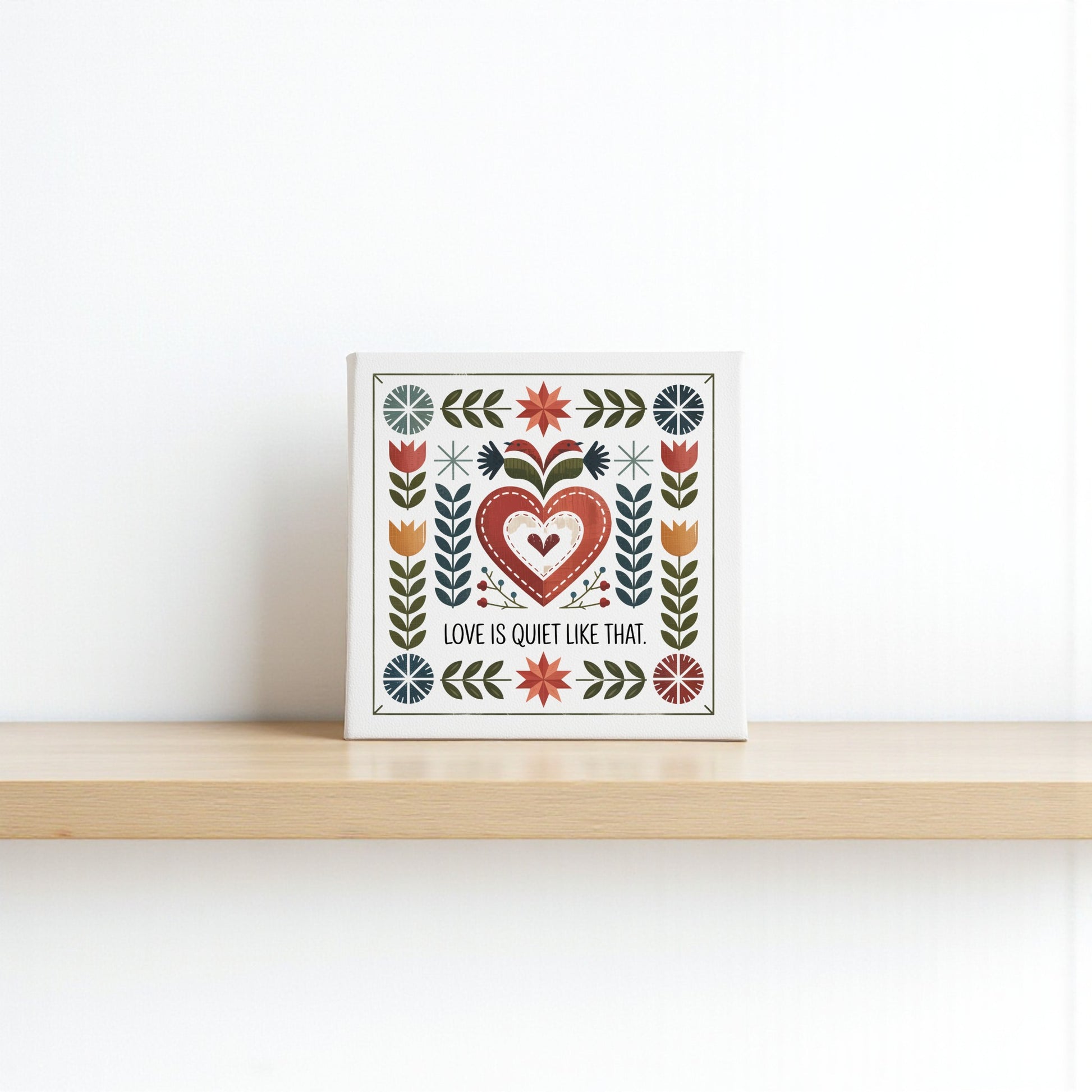 The Mirabilia Boutique "Love Is Quiet Like That Canvas" features a folk art heart and floral design on a white background, perfect for adding charm to your cozy decor. Ideal as a wall decor gift for any home.