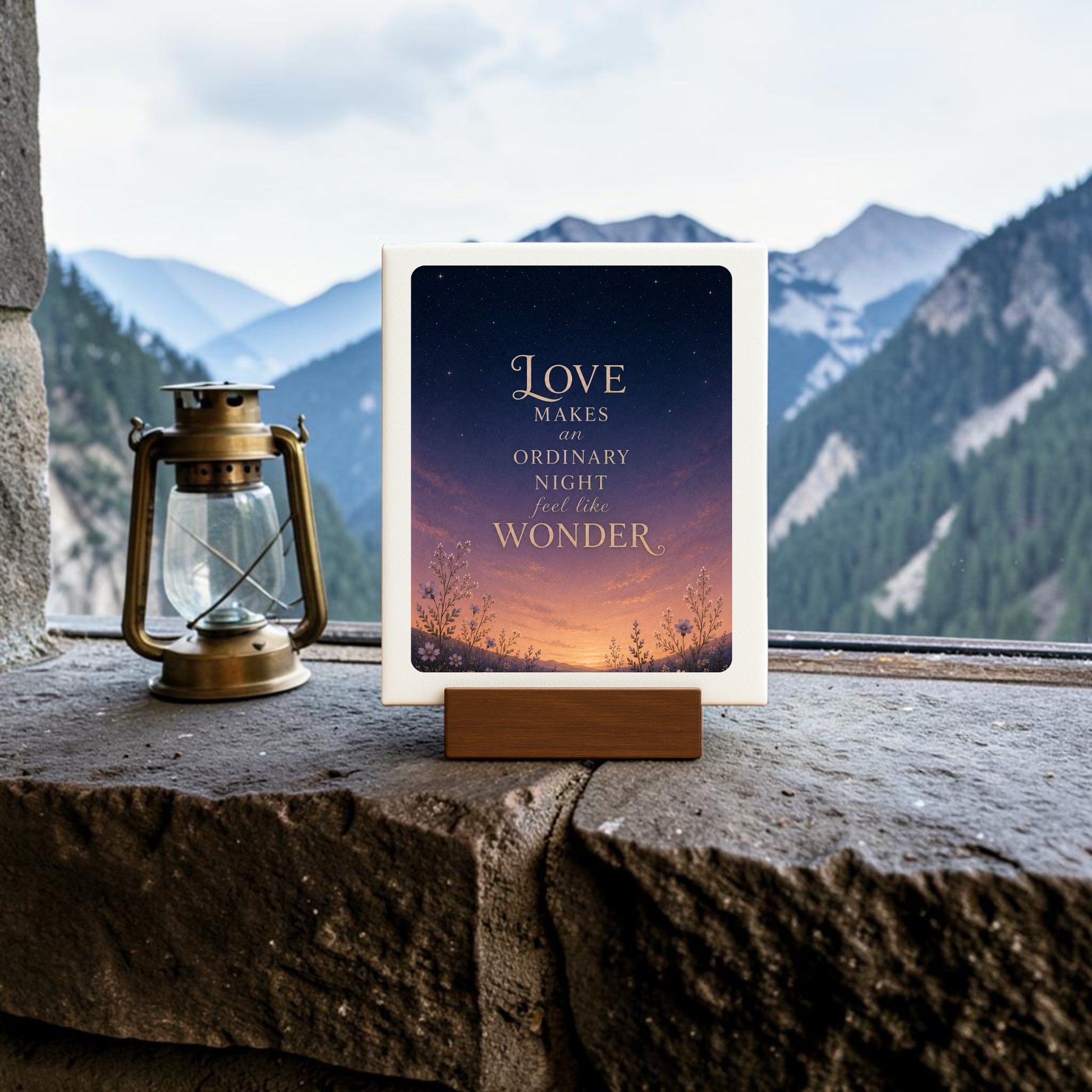 A decorative sign from Mirabilia Boutique’s Celestial Decor collection sits on a stone ledge, reading “Love makes an ordinary night feel like wonder,” with a lantern nearby and mountains visible through the window—a charming piece titled Love Makes Wonder Romantic Mini Sign.