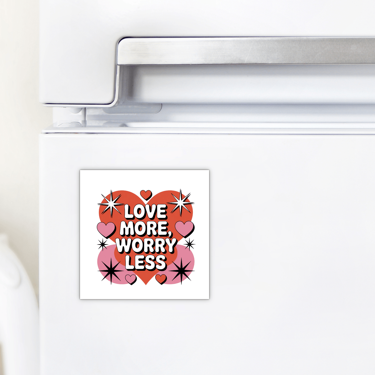 The Love More Worry Less Magnet by Mirabilia Boutique is a cute, retro Valentine fridge decor with "Love More, Worry Less," red and pink hearts, and black starbursts on a white background.