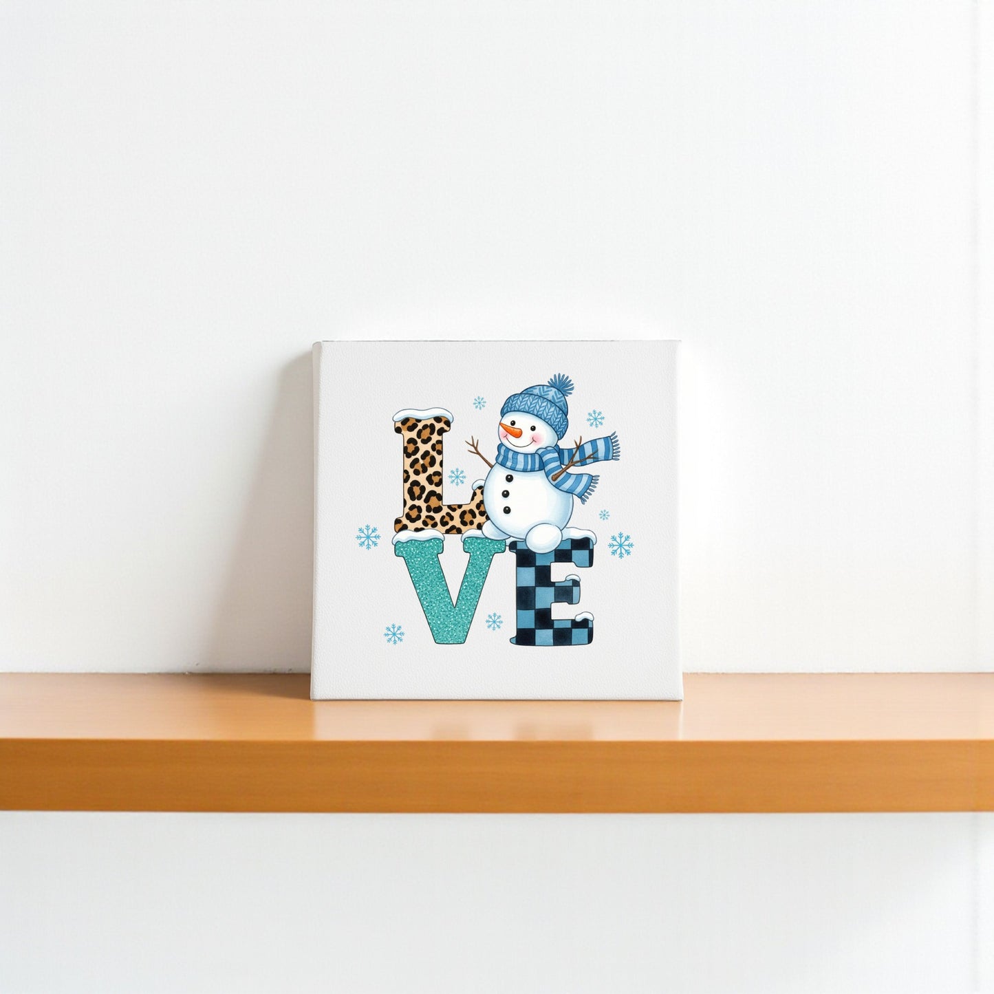 The LOVE Snowman Canvas Sign by Mirabilia Boutique features patterned letters with a snowman “O” in a blue hat and scarf—perfect as winter or Valentine’s decor for brightening any white-walled space.