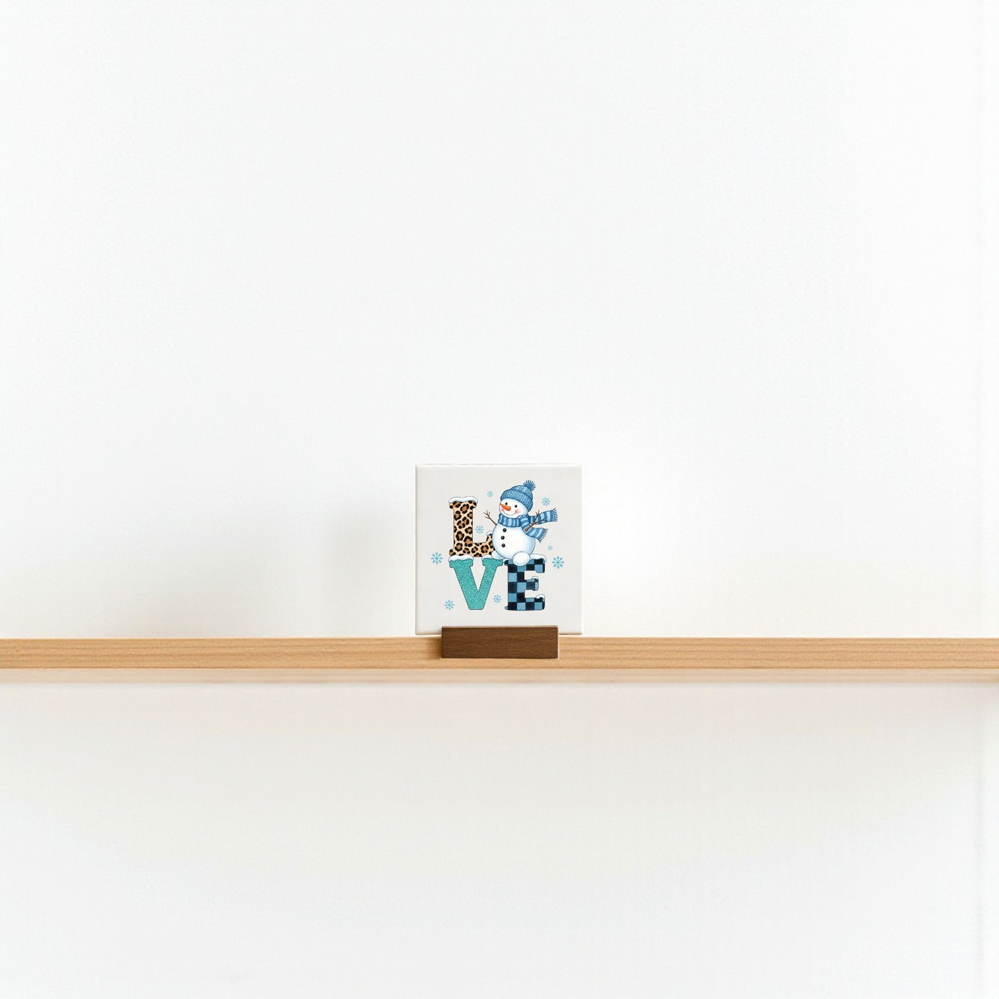 The Mini LOVE Snowman Sign by Mirabilia Boutique is a 4x4 decorative block featuring "LOVE" with a snowman as the "O"—a charming winter Valentine decor piece, ideal for minimalist shelf displays.