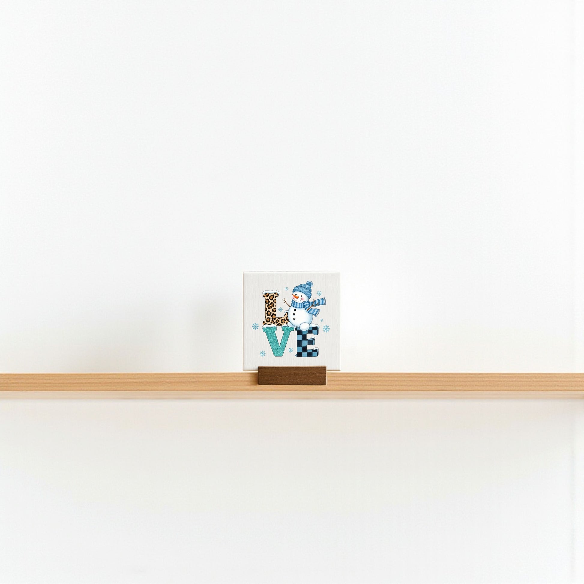 The Mini LOVE Snowman Sign by Mirabilia Boutique is a 4x4 decorative block featuring "LOVE" with a snowman as the "O"—a charming winter Valentine decor piece, ideal for minimalist shelf displays.