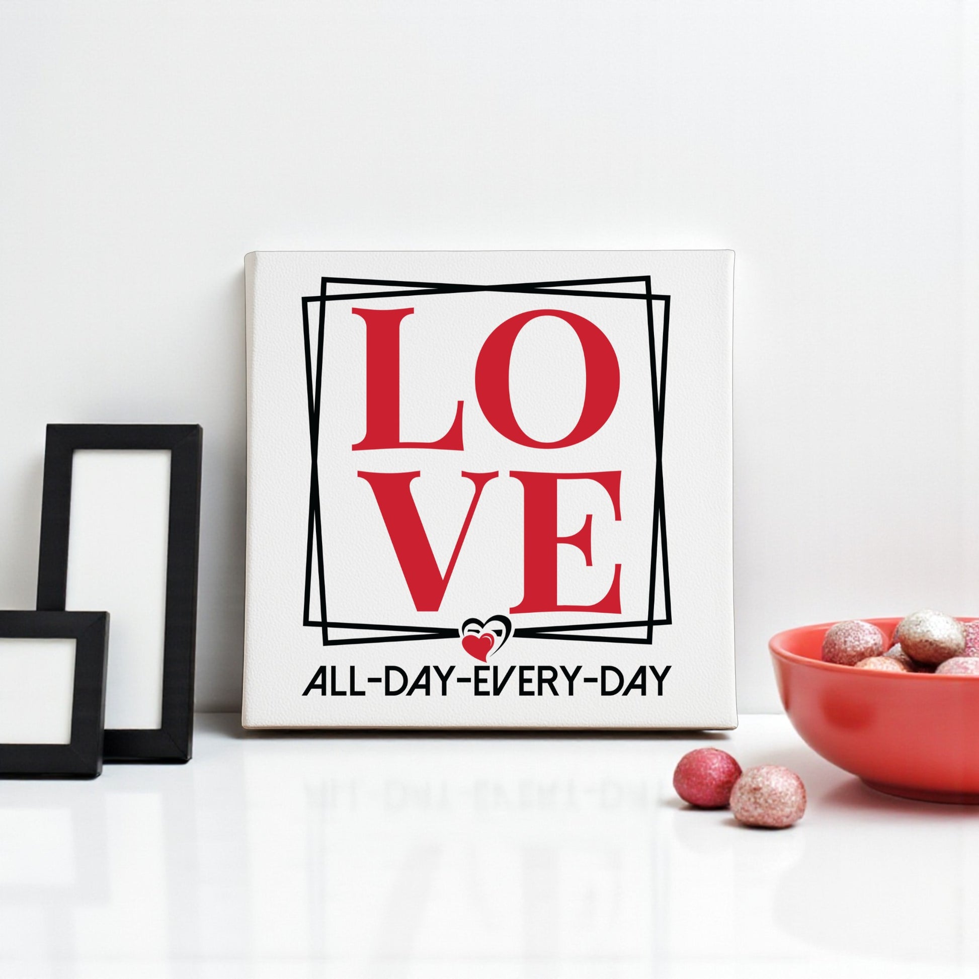 The Love Wall Art Print by Mirabilia Boutique features bold red letters above "ALL DAY EVERY DAY," making a romantic, modern decor piece—perfect with minimalist accents like black frames and a red decorative bowl.