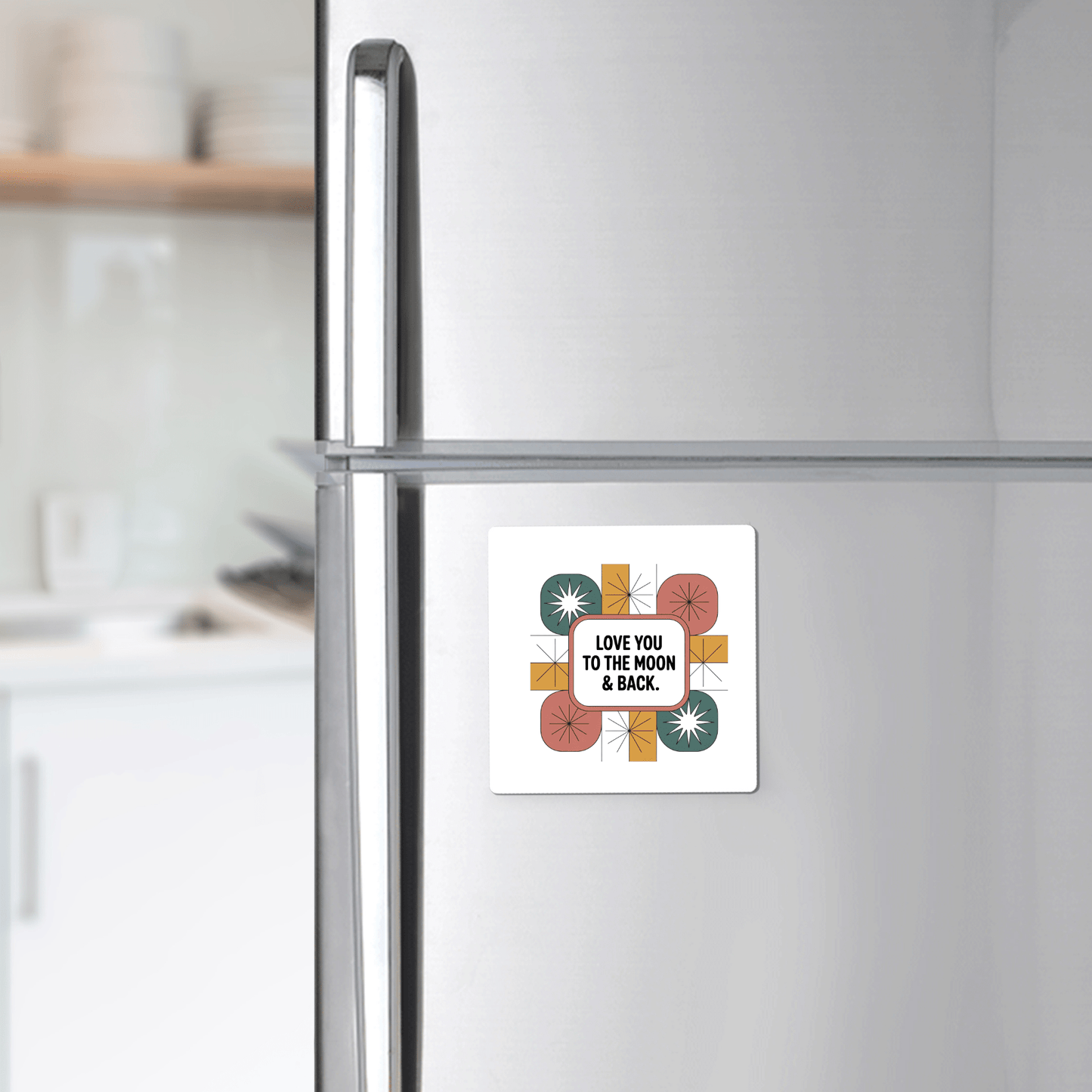 The Mirabilia Boutique Retro Love Magnet, reading "LOVE YOU TO THE MOON & BACK," adds a charming touch to a stainless steel fridge in a modern kitchen, with shelves of dishes visible in the background.