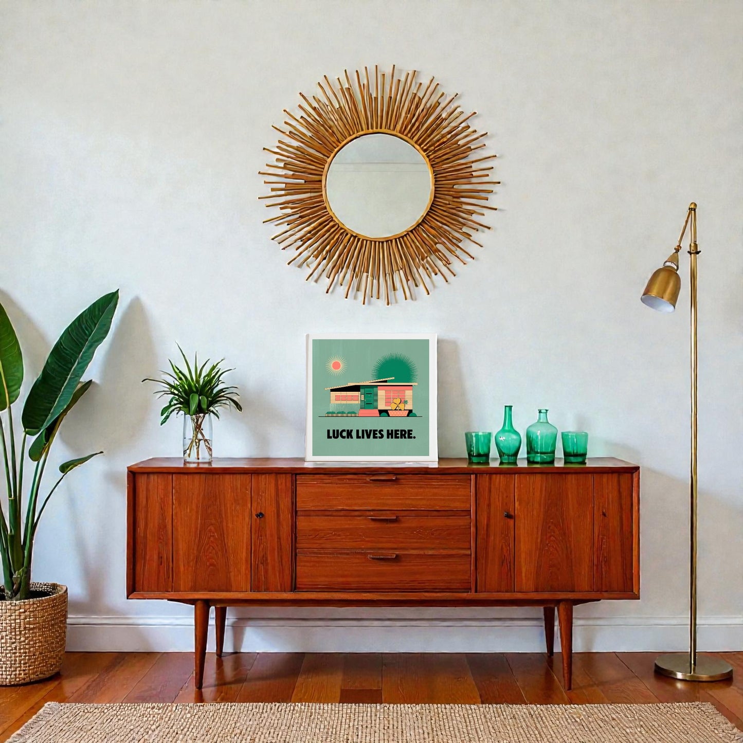 A mid-century modern sideboard with green glass decor, a potted plant, and Mirabilia Boutique's Luck Lives Here Canvas Sign stands below a sunburst mirror beside a brass floor lamp in this stylish living room.