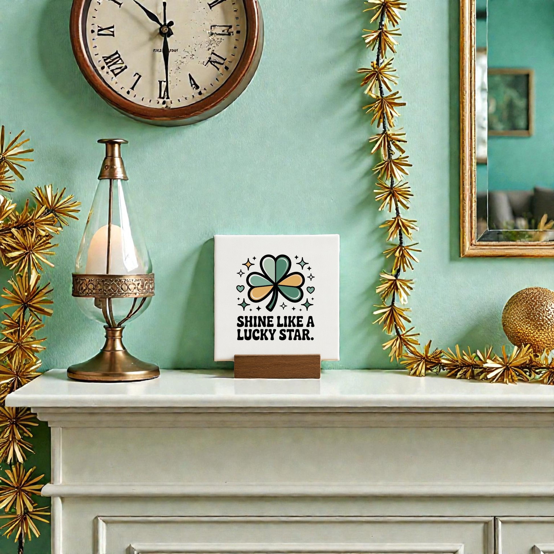 A mantel adorned with gold star garland, a lamp, and the Mirabilia Boutique “Shine Like a Lucky Star” 4x4 Canvas Sign sits beneath a clock, beside a gold ball and framed mirror on a green wall for St. Patrick’s Day flair.