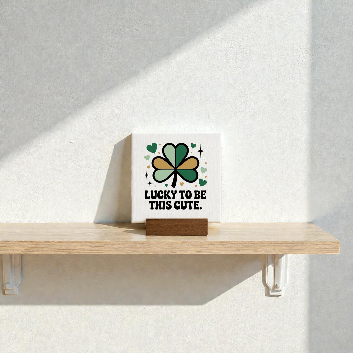 The Lucky to Be This Cute Canvas Sign – 4x4 by Mirabilia Boutique features green, black, and gold shamrocks and hearts with the phrase "Lucky to be this cute." Ideal clover decor or St. Patrick’s Day gift for shelves or nurseries.