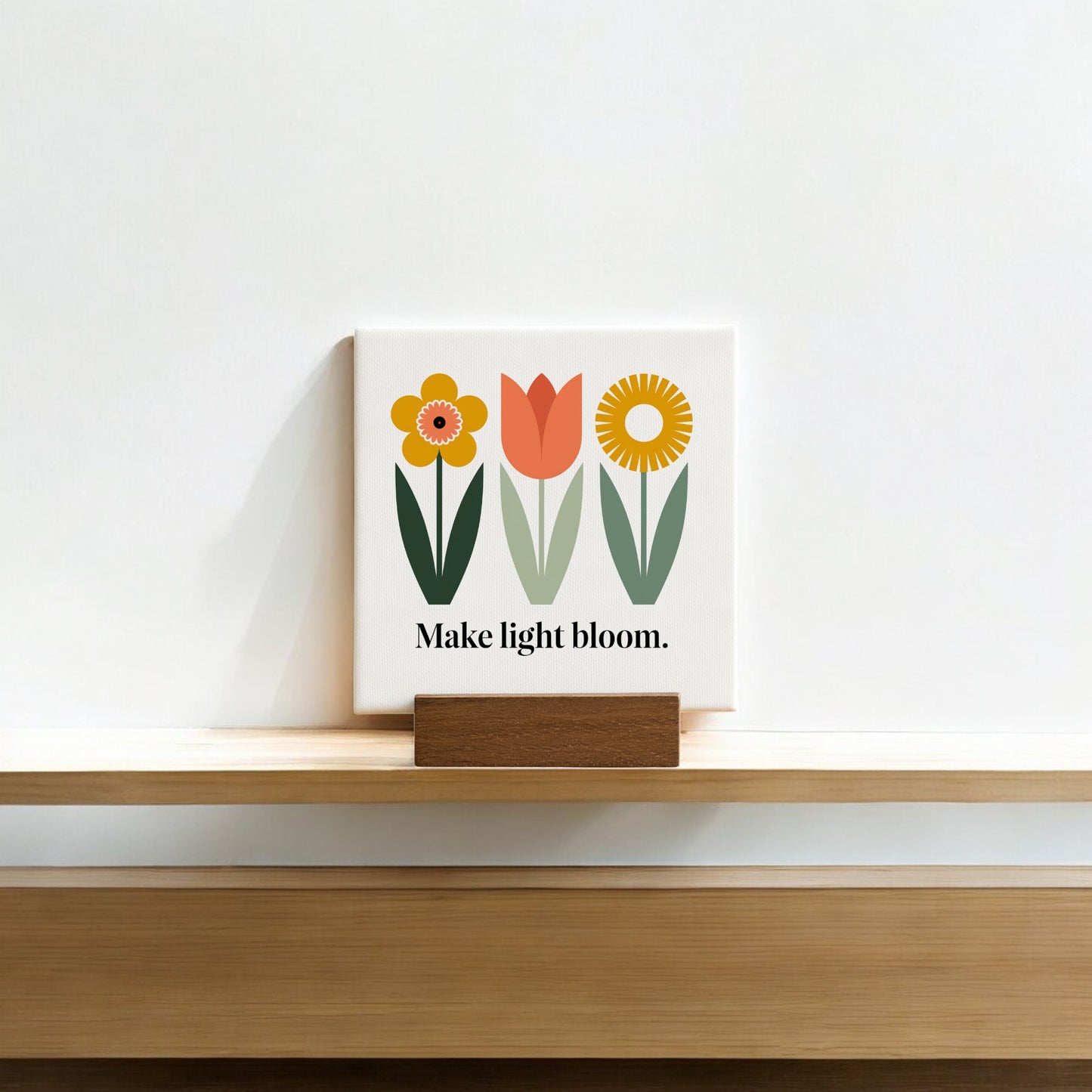 The Make Light Bloom Mini Canvas Sign with Wood Base by Mirabilia Boutique features simple floral art and the phrase “Make light bloom.”—an ideal daily affirmation or charming decor for small spaces.