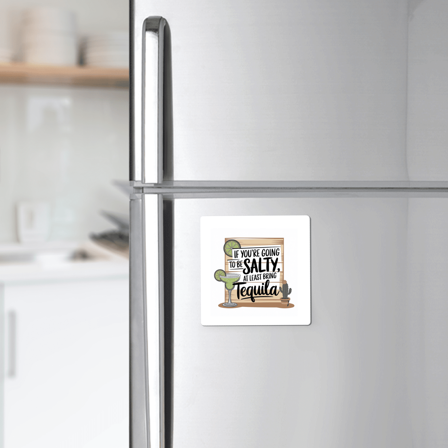 The Salty Tequila Magnet by Mirabilia Boutique, featuring a funny margarita quote and cactus design, adds charm to a stainless steel fridge with white shelves and dishes in the background.