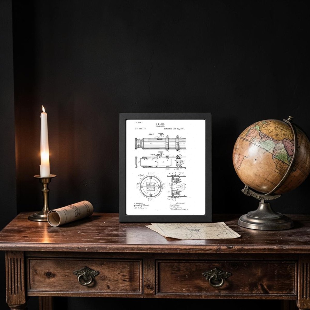 A lit candle, the Mirabilia Boutique Nautical Telescope Patent Art Print in a frame, a globe, and rolled papers sit on a dark wood desk against a black wall, evoking an antique, scholarly vibe with refined maritime decor.