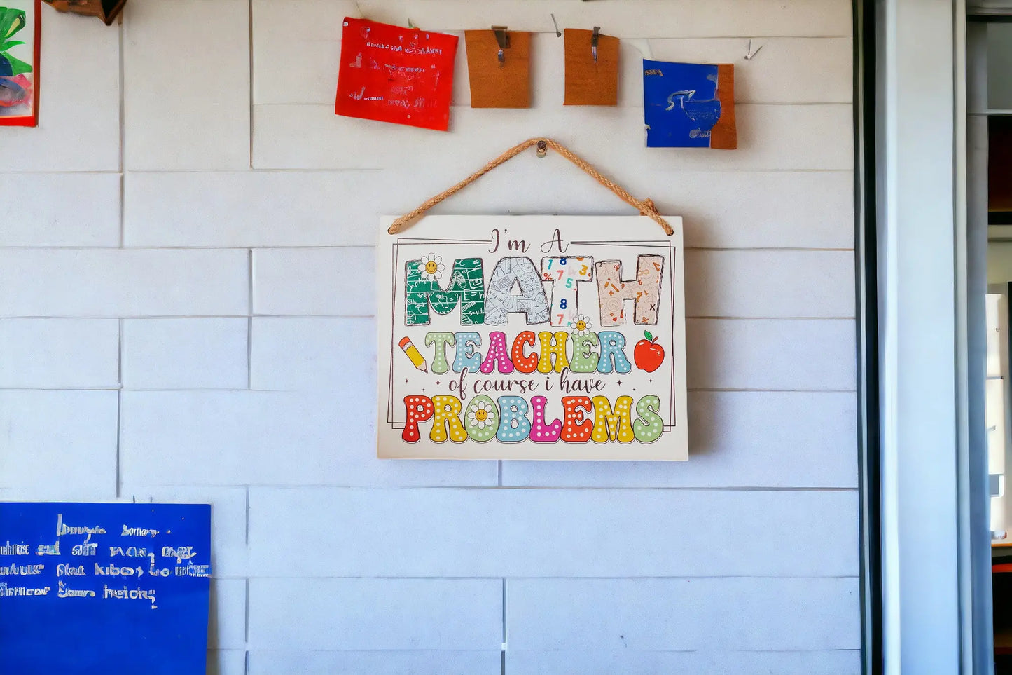 A vibrant wall sign from Mirabilia Boutique, called "I'm a Math Teacher: Humorous Problems Hanging Sign," amusingly reads, "Of course I have problems." Art and notes are thoughtfully arranged above and below this humorous decor piece.
