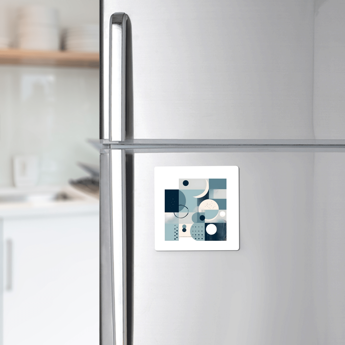 A Moonlit Geometry Mid Century Modern Magnet by Mirabilia Boutique, with abstract blue, white, and gray shapes, is displayed on a silver refrigerator in a modern kitchen.