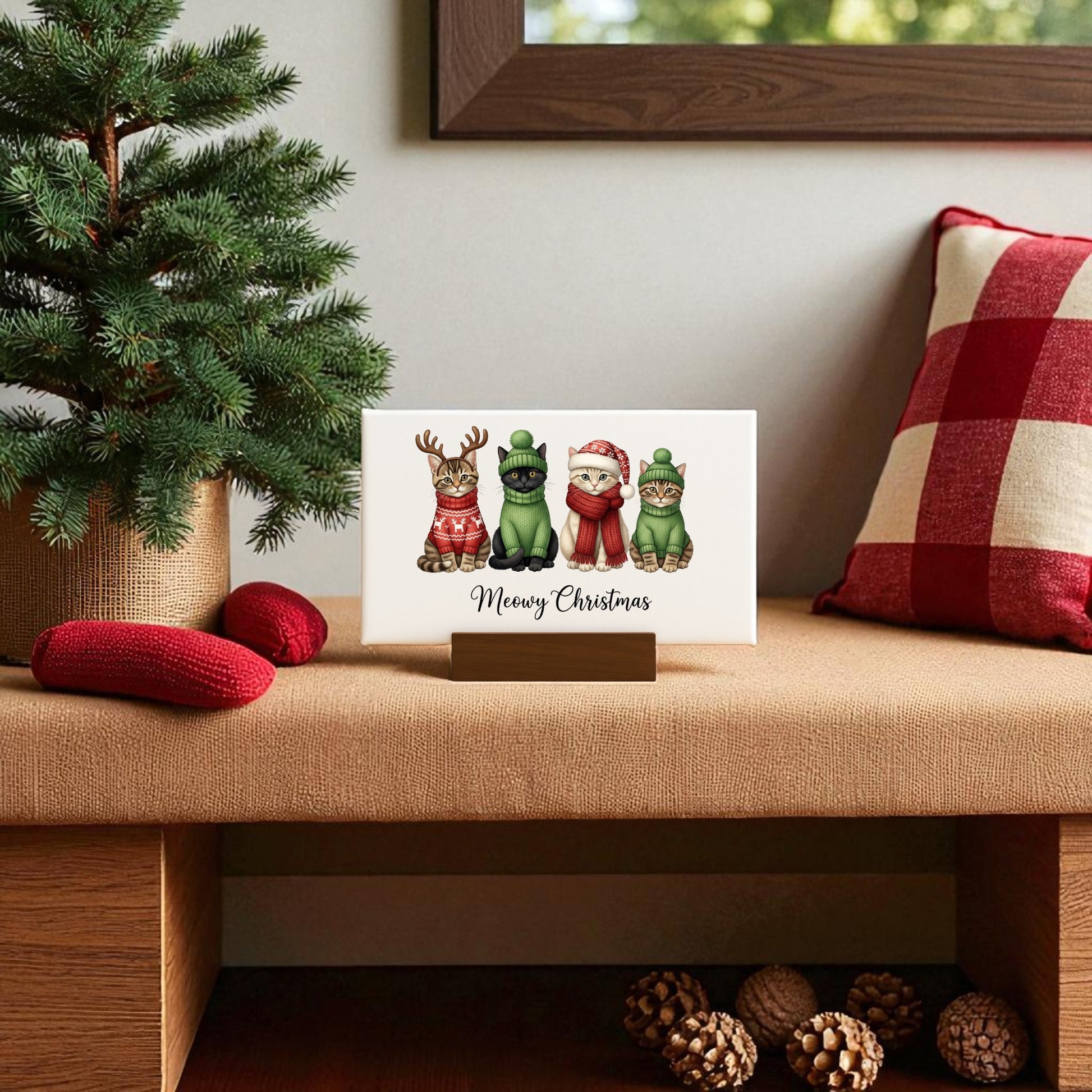 The Meowy Christmas Cat Sign by Mirabilia Boutique is displayed on a wooden stand near festive decor—a cute mini canvas holiday gift, perfect for cat lovers and cozy home accents.