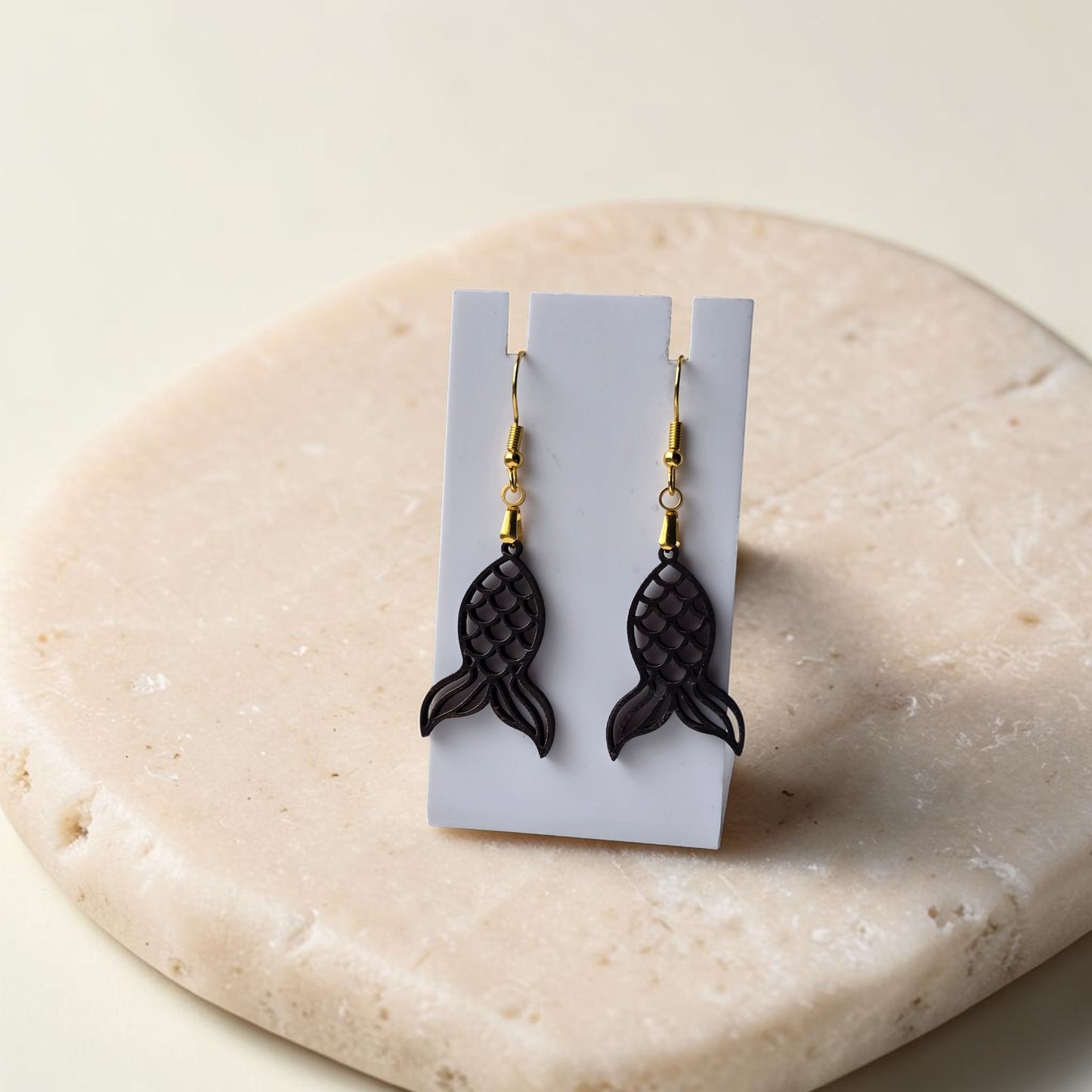 Mermaid Tail Earrings by Mirabilia Boutique—crafted from lasercut walnut wood with gold hooks, displayed on a white card atop a beige stone surface. Perfect for coastal jewelry lovers.