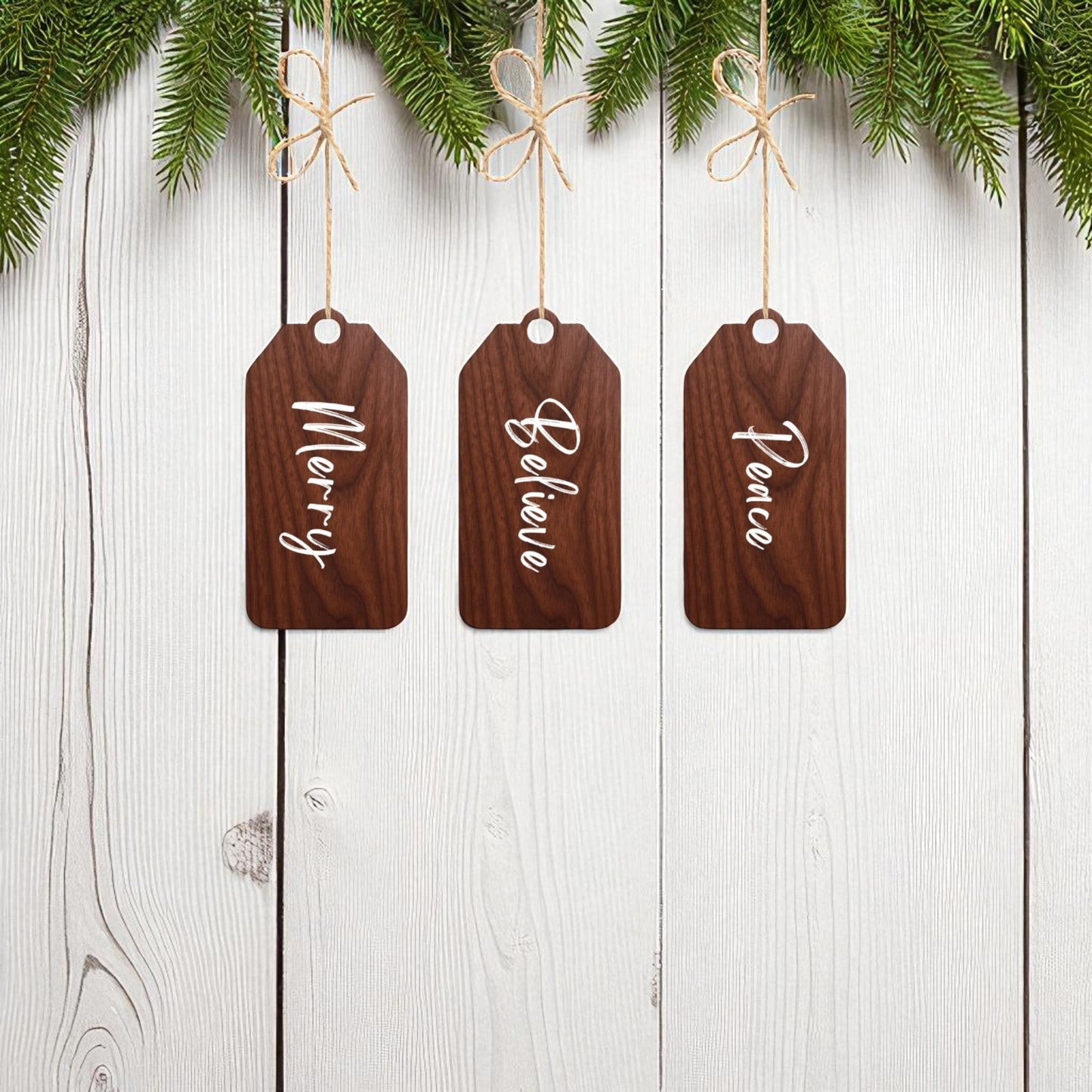 Mirabilia Boutique’s Merry Believe Peace Tags set features three 5x2 rustic wood ornaments with festive sayings, hanging from strings under evergreen branches for charming Christmas décor.