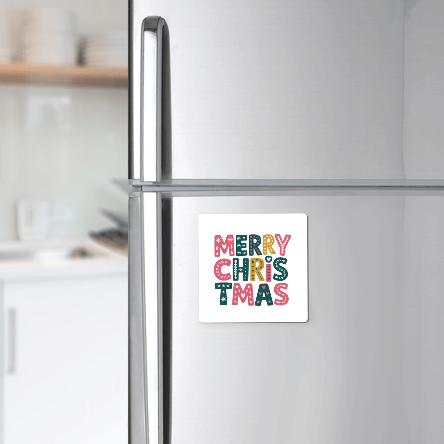 The Mirabilia Boutique Merry Christmas Magnet adds festive, colorful holiday cheer to your silver refrigerator, making it a perfect decor piece for modern kitchens with white shelves and dishes.
