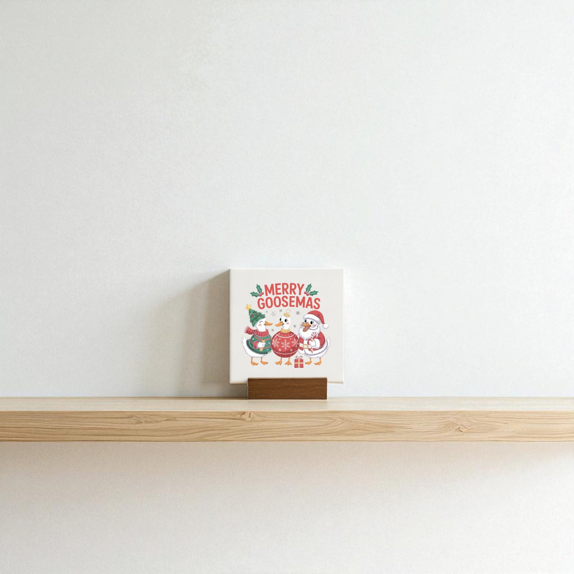 The Merry Goosemas Mini Sign by Mirabilia Boutique features cartoon geese and “Merry Goosemas,” displayed on a wooden easel—perfect as a funny holiday gift or whimsical decor to brighten any shelf or desk.