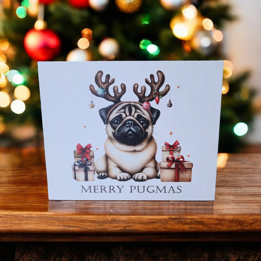 The "Merry Pugmas 10x8 Canvas Sign" from Mirabilia Boutique depicts an adorable holiday scene with a pug wearing reindeer antlers, sitting between wrapped gifts on a wooden table. The festive text reads "Merry Pugmas," and a Christmas tree adorned with colorful ornaments is beautifully blurred in the background, making it ideal for holiday decor or as a delightful addition to any wall.