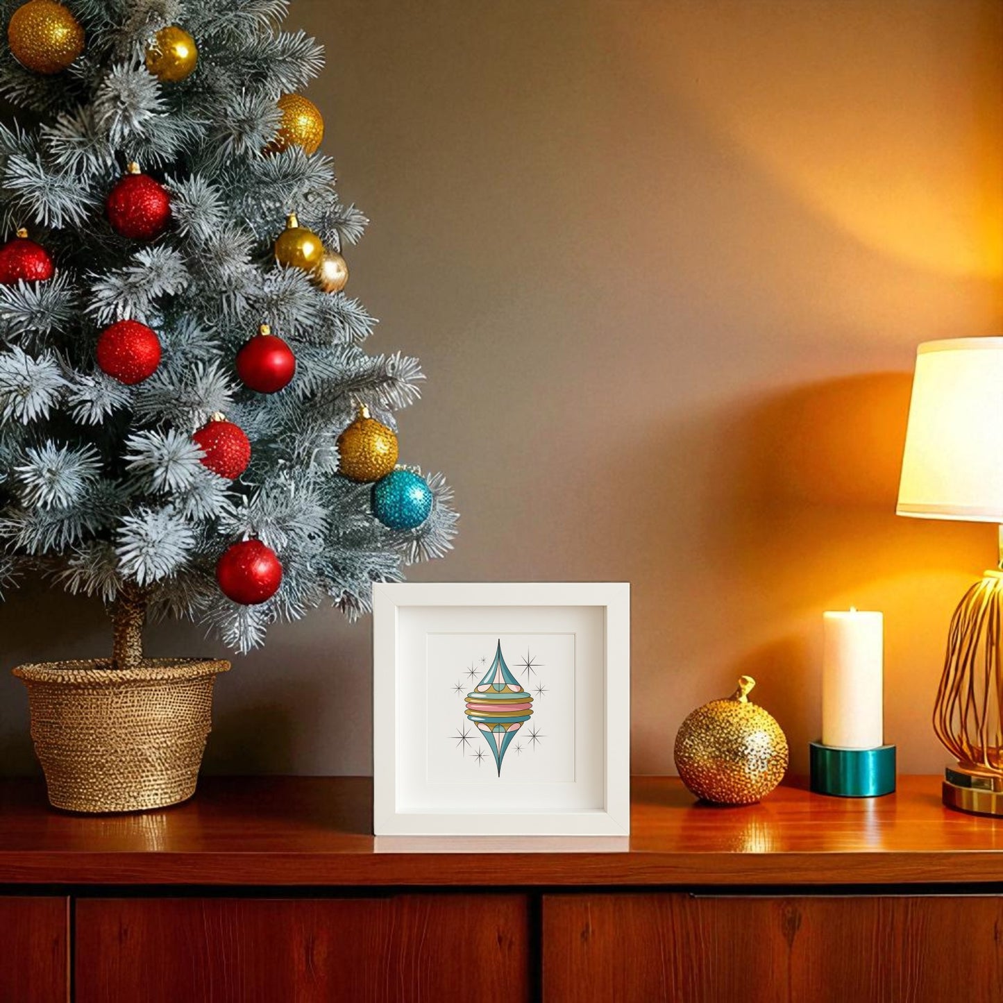 A decorated Christmas tree sits on a wooden table beside a lamp, candle, gold ornament, and framed Retro Icicle Ornament Art | Mid-Century Christmas Shadowbox by Mirabilia Boutique, adding festive mid-century flair.