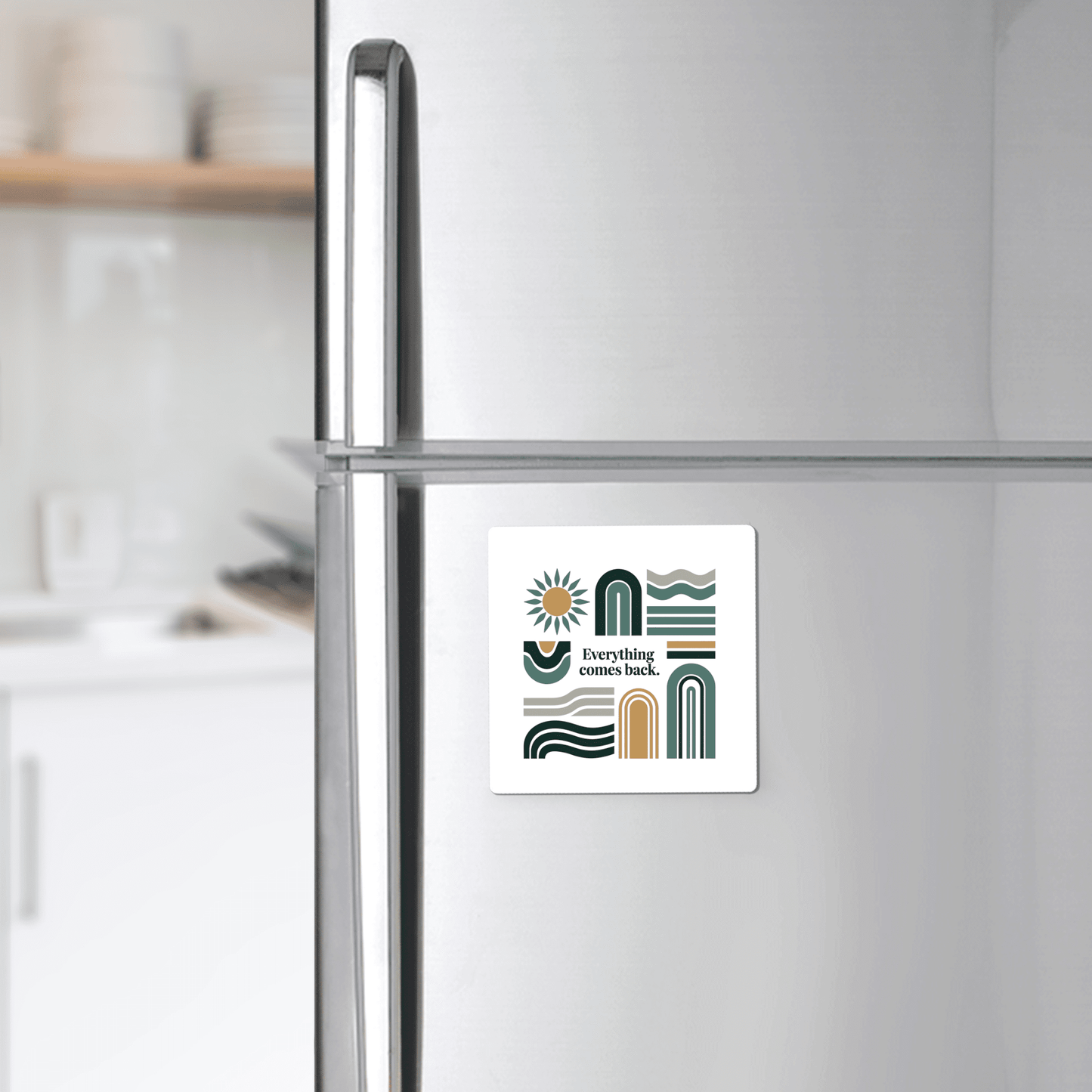 The Everything Comes Back Magnet – Earth Tone Affirmation by Mirabilia Boutique, with abstract green and gold shapes and inspiring text, adds calming decor to a stainless steel refrigerator in a modern kitchen.