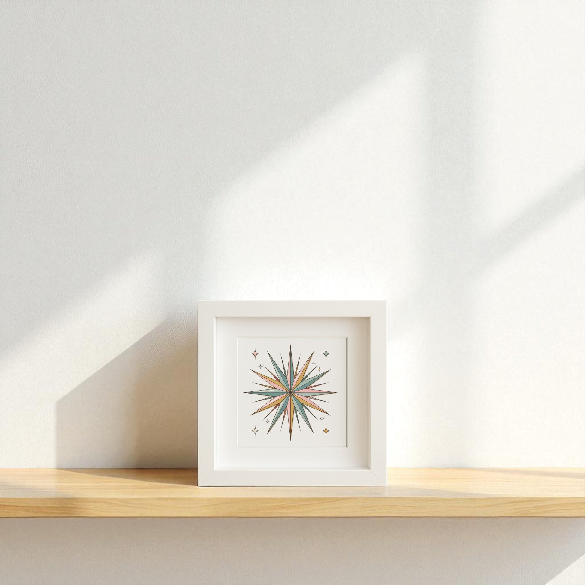 The Atomic Starburst Ornament Art by Mirabilia Boutique rests on a light wooden shelf against a white wall, sunlight casting soft shadows and enhancing the calm, minimalist vibe with retro holiday shadowbox style.
