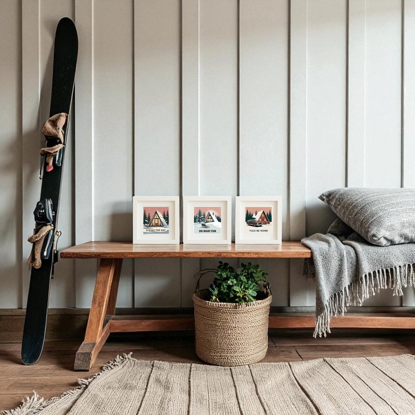 A wooden bench displays the Mirabilia Boutique Mid-Century Modern A-Frame Cabin Sign Trio | Sleigh the Day Set. Below is a woven basket with a plant, while a gray blanket, cushion, and ski rest nearby against the paneled wall.