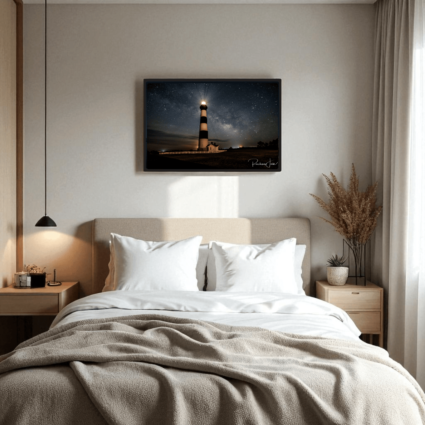 A cozy bedroom with a neatly made bed, light bedding, wooden nightstands, a hanging lamp, dried plant décor, and Mirabilia Boutique’s "Milky Way at Bodie Lighthouse | Framed Art Print | Outer Banks Nightscape" above the bed.