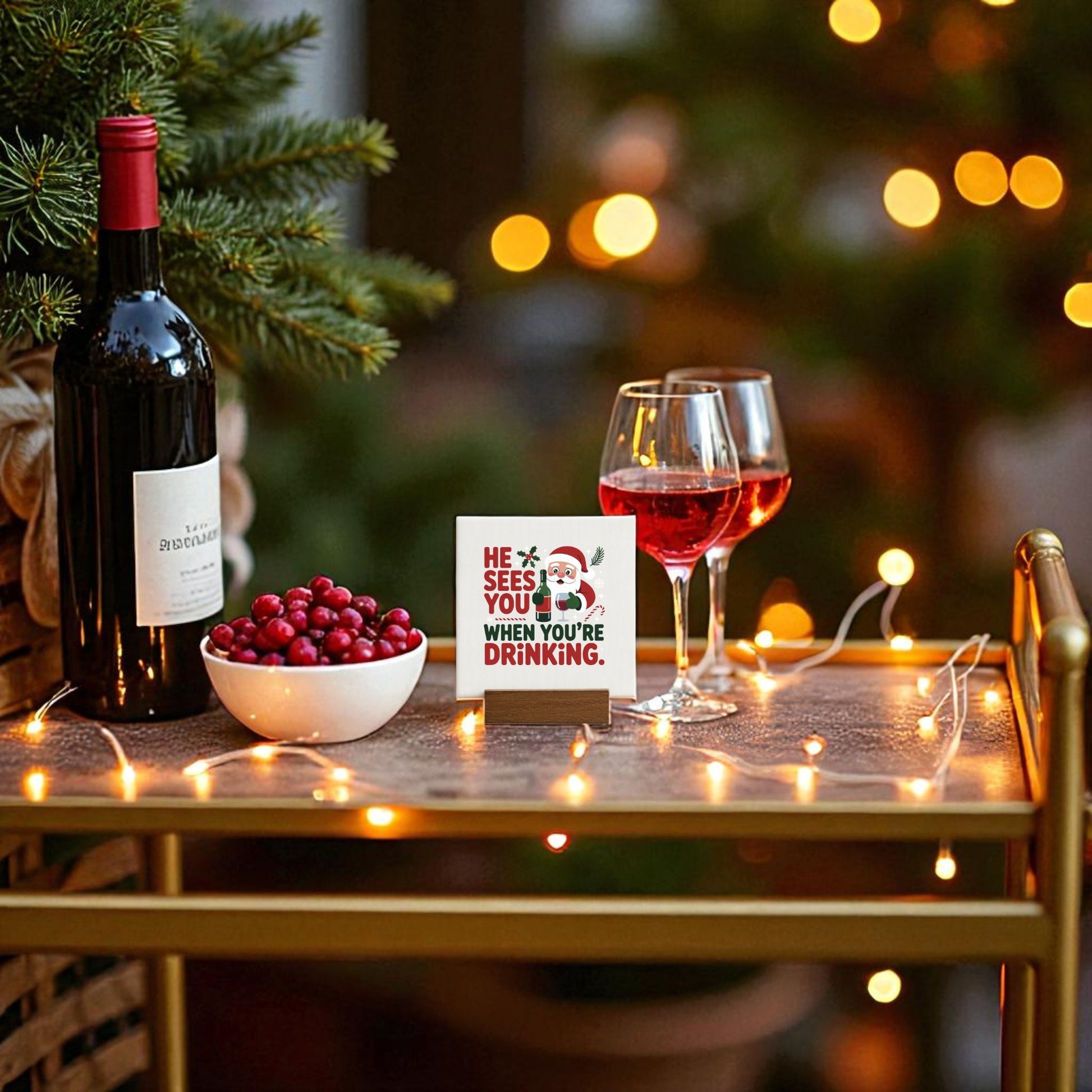 A festive bar cart displays Mirabilia Boutique’s “He Sees You When You’re Drinking” funny mini Christmas sign with Santa, a bottle of red wine, glasses, cranberries, and string lights—the perfect holiday décor for wine lovers.
