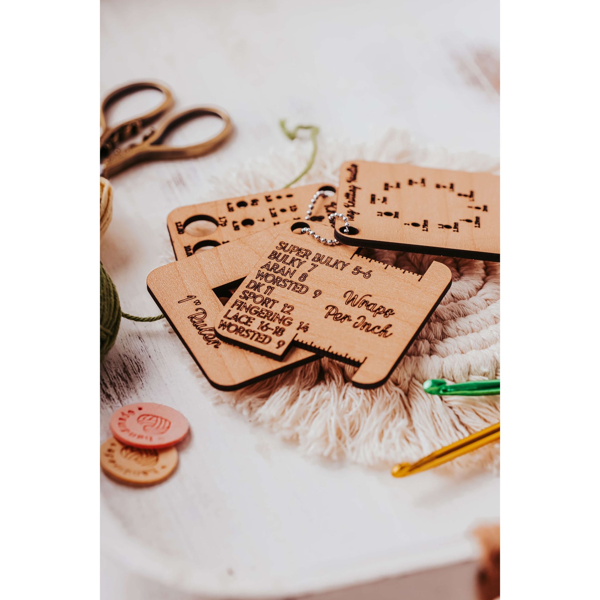 The Knitter’s Pocket Tool Set from Mirabilia Boutique, elegantly showcased on a white surface, features wooden keychains with yarn size details. It includes scissors and crochet hooks, making it perfect for travel knitting accessories or as a gift in project bags.