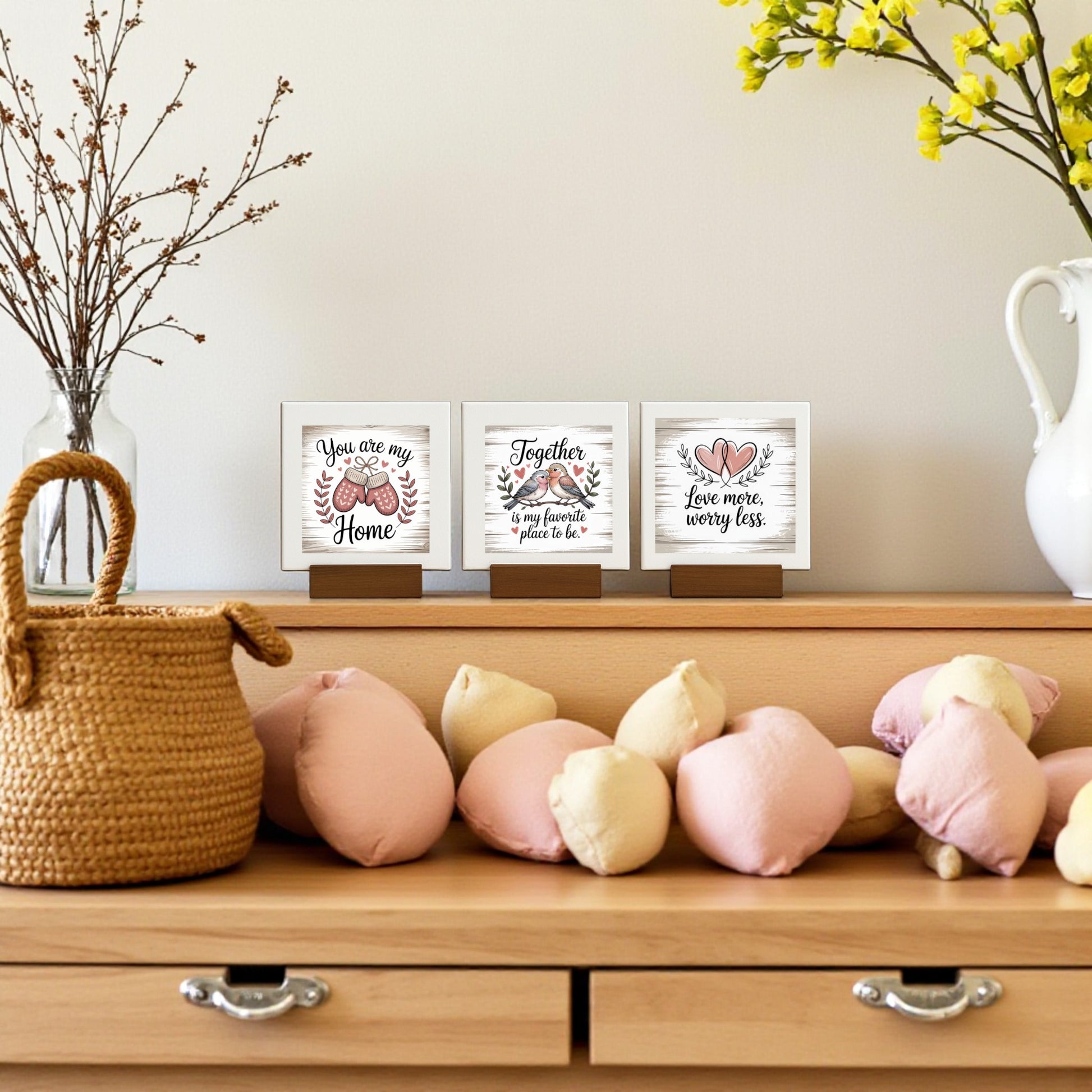 A wooden dresser displays heart-shaped pillows, a woven basket, and the Mirabilia Boutique Mini Love Quote Sign Trio. A white vase with yellow flowers completes this charming farmhouse decor scene.