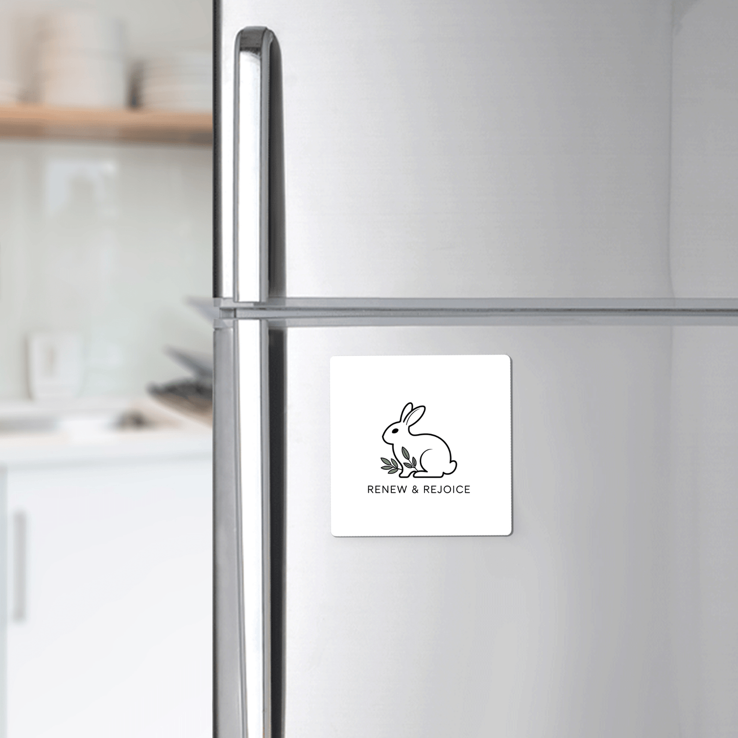 The Renew & Rejoice Magnet – Minimalist Bunny Design by Mirabilia Boutique, ideal for Easter basket fillers or mindfulness reminders, is displayed on a stainless steel fridge in a modern kitchen.