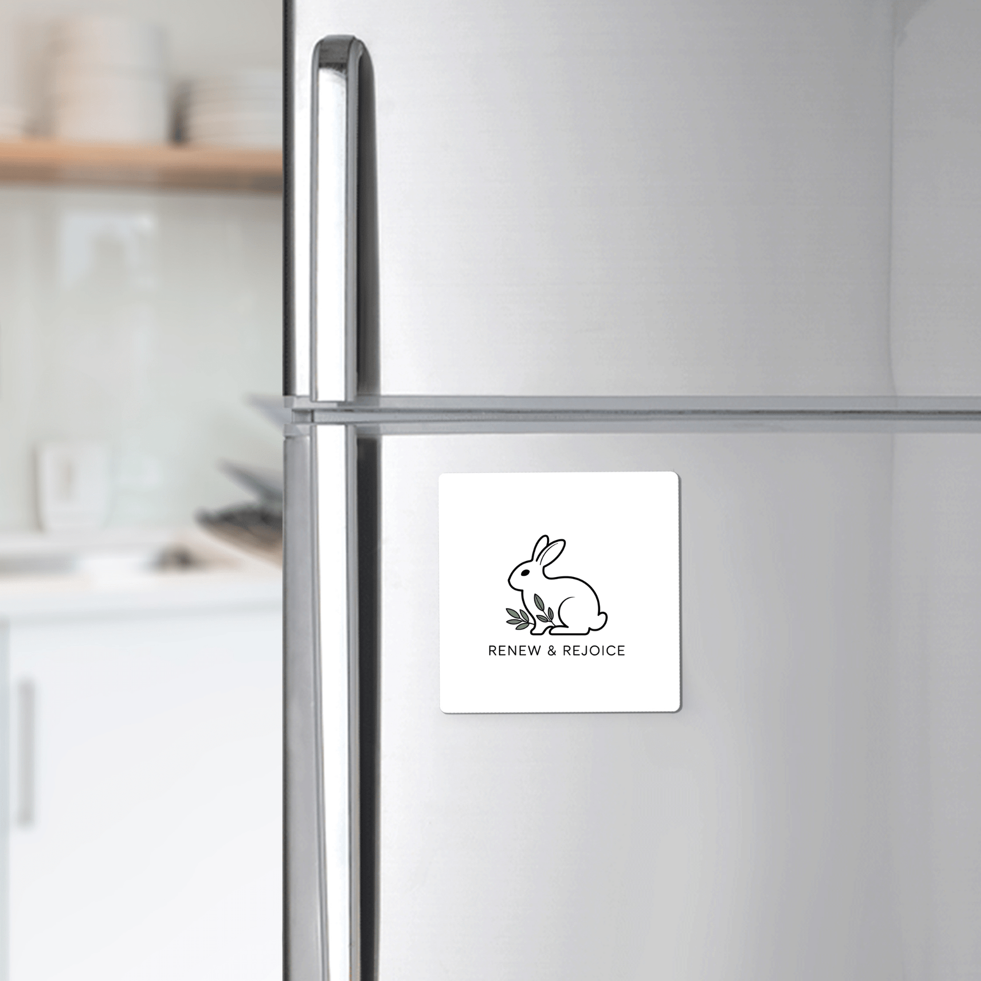 The Renew & Rejoice Magnet – Minimalist Bunny Design by Mirabilia Boutique, ideal for Easter basket fillers or mindfulness reminders, is displayed on a stainless steel fridge in a modern kitchen.