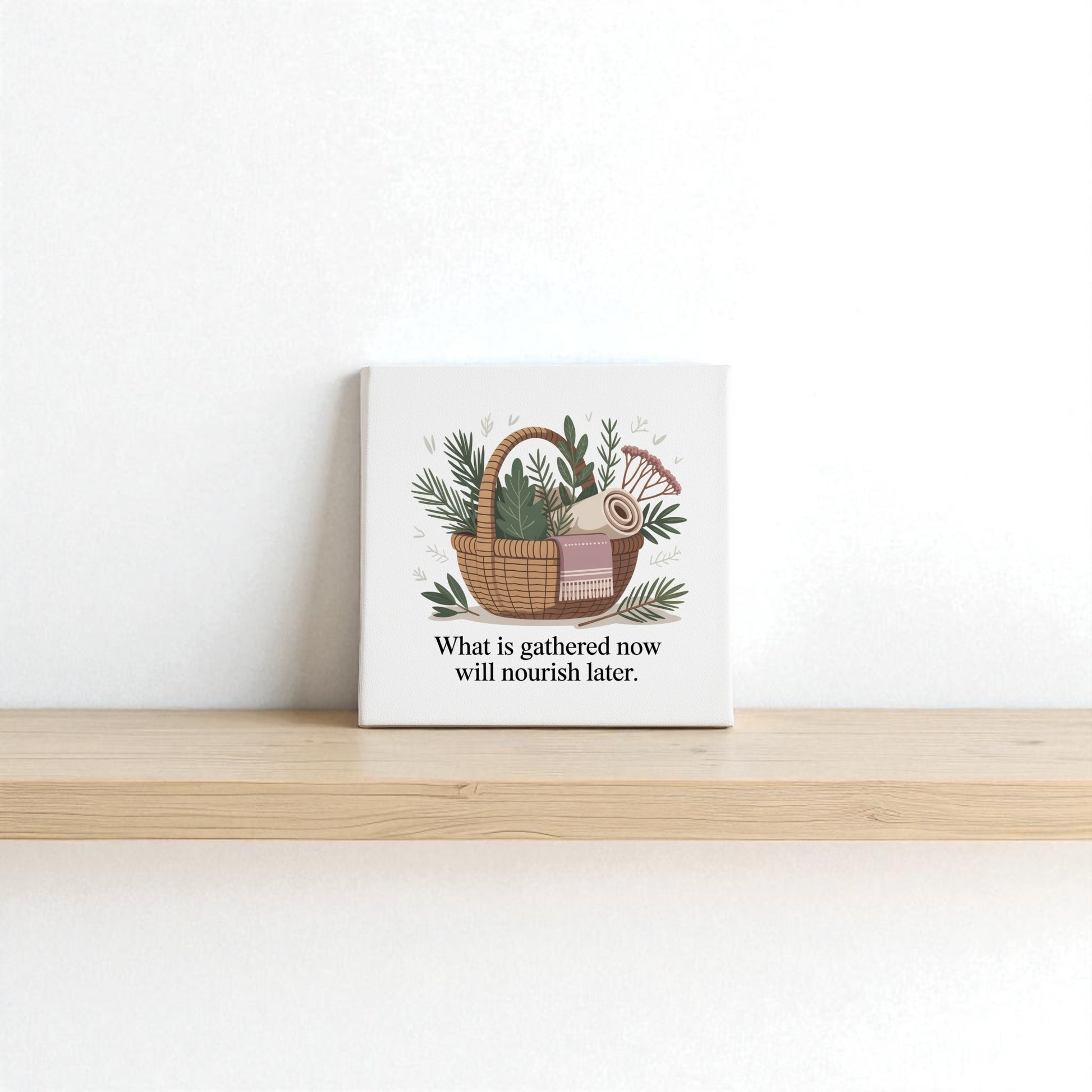 The Herbal Basket Canvas Art by Mirabilia Boutique features a woven basket with greenery and a blanket, plus the quote “What is gathered now will nourish later”—a mindful, seasonal touch for your home décor.