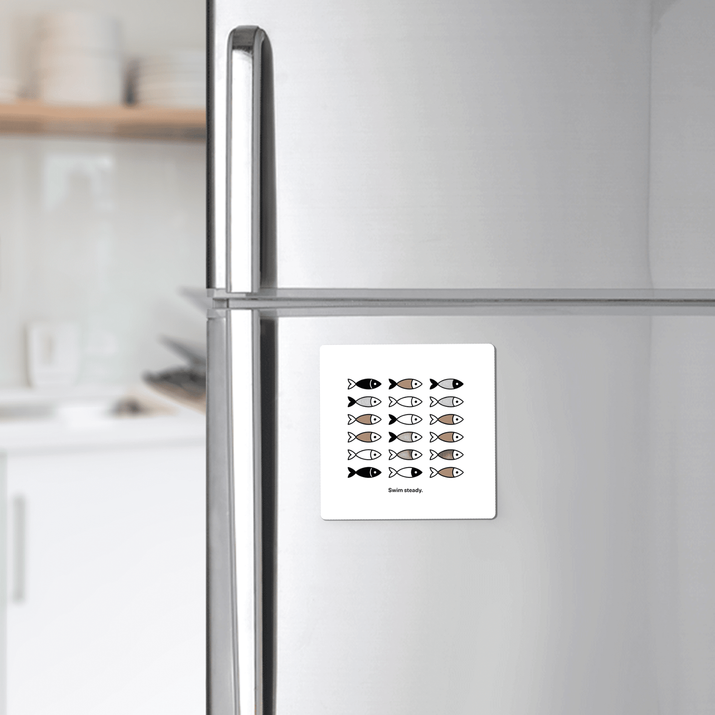 A silver fridge in a modern kitchen displays the Swim Steady Magnet – Minimalist Motivational Fridge Art by Mirabilia Boutique, featuring black fish and one gold fish swimming opposite, with "Swim nicely" below—ideal for minimalist decor.