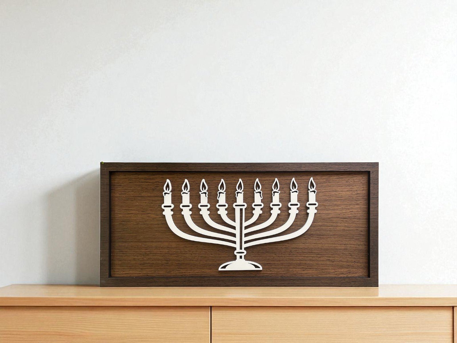 The Minimalist Menorah Decor | 9x4 Laser Cut Hanukkah Sign by Mirabilia Boutique features a wooden frame and white silhouette of a nine-branched menorah—perfect Hanukkah decor for your home.