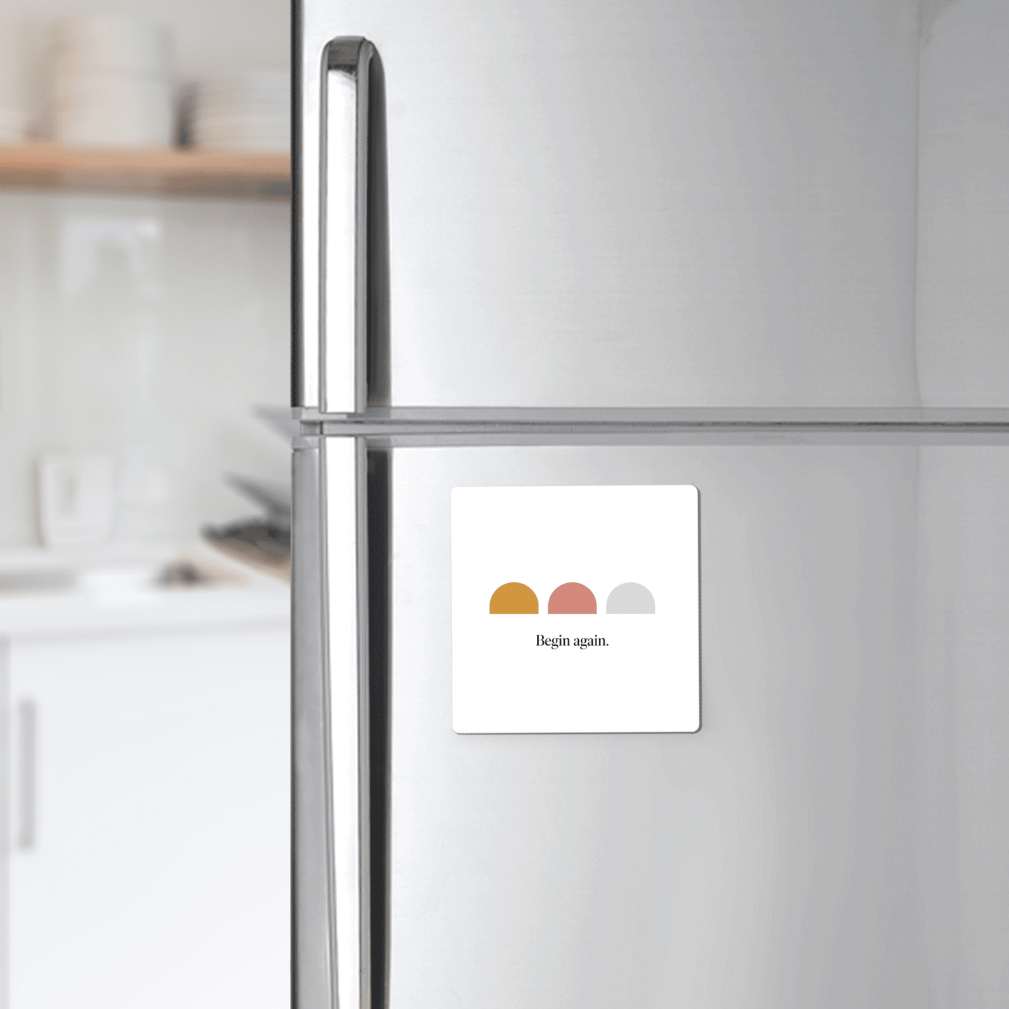 The Begin Again Magnet – Minimalist Summer Affirmation by Mirabilia Boutique decorates a white fridge with three colored semicircles and the phrase "Begin again," adding a daily dose of inspiration to your kitchen.