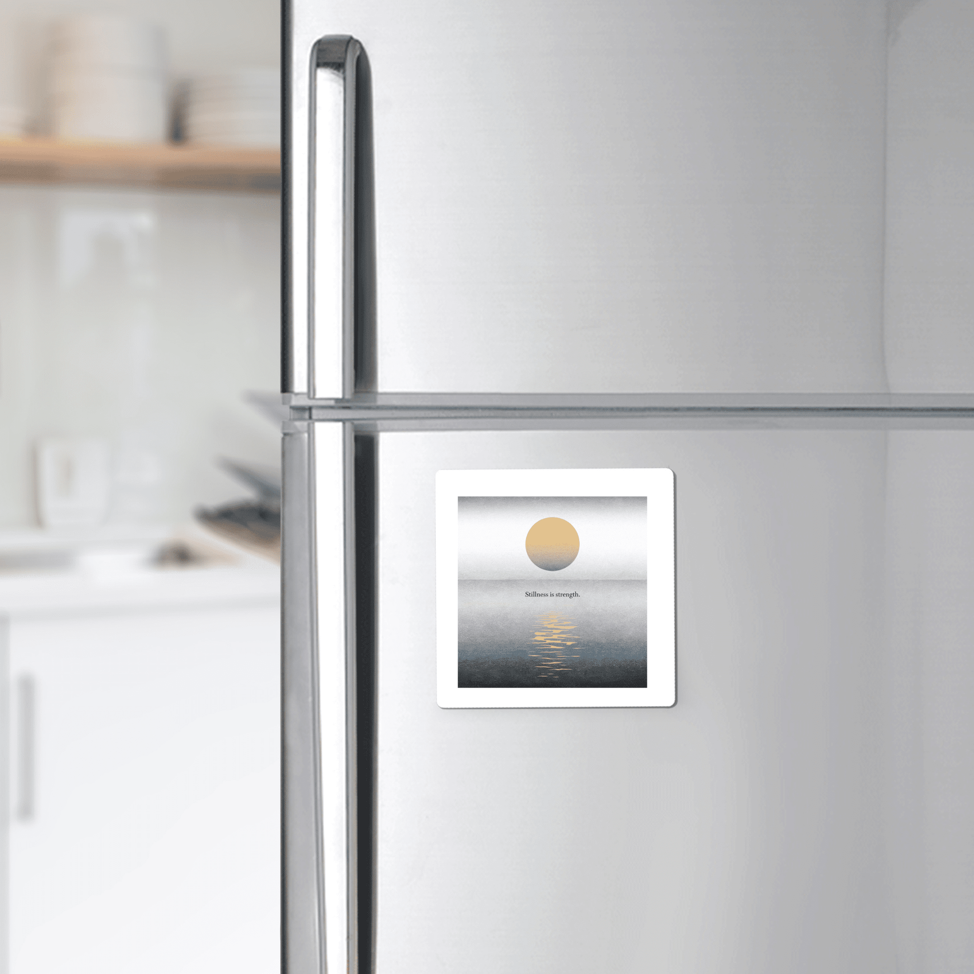 The Stillness Is Strength Magnet by Mirabilia Boutique, featuring a minimalist sun-over-water design, adds calm and warmth to your modern kitchen decor. Perfect for mindful gifting, it’s shown on a stainless steel fridge with dishes in view.