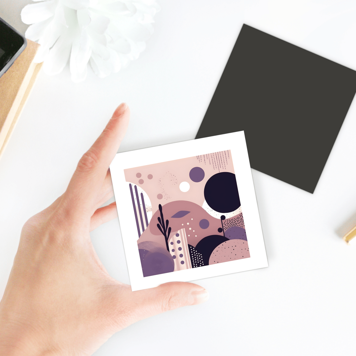 A hand holds the Purple Dusk Mid Century Modern Magnet by Mirabilia Boutique, featuring abstract art in muted pink, purple, and beige tones—perfect inspiration for stylish desks and decor lovers.