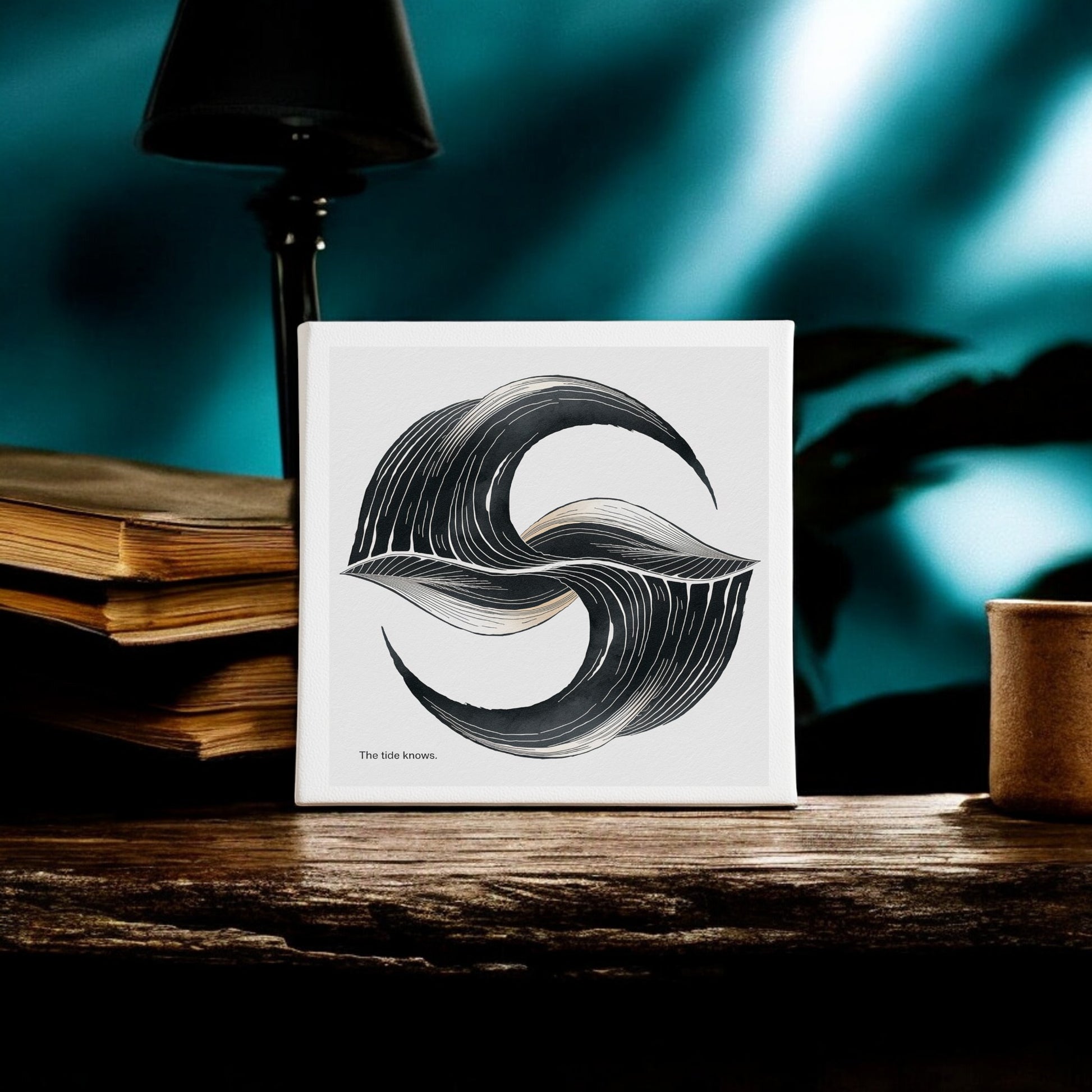 The Tide Knows Canvas by Mirabilia Boutique, an 8x8 abstract coastal wall art, features a minimalist black and white wave design displayed on a rustic wooden table beside stacked books and a cup, set against a blurred blue background.