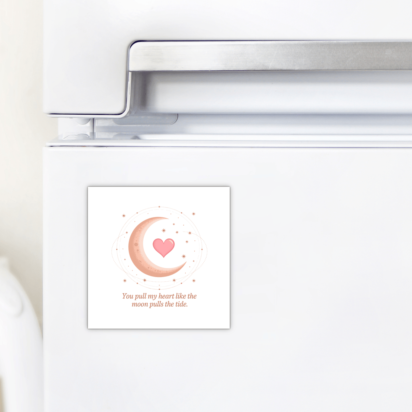 A white fridge with the Mirabilia Boutique Moon and Heart Love Quote Magnet, featuring a pink crescent moon, heart, stars, and the phrase “You pull my heart like the moon pulls the tide”—ideal as a romantic gift or moon heart decor.