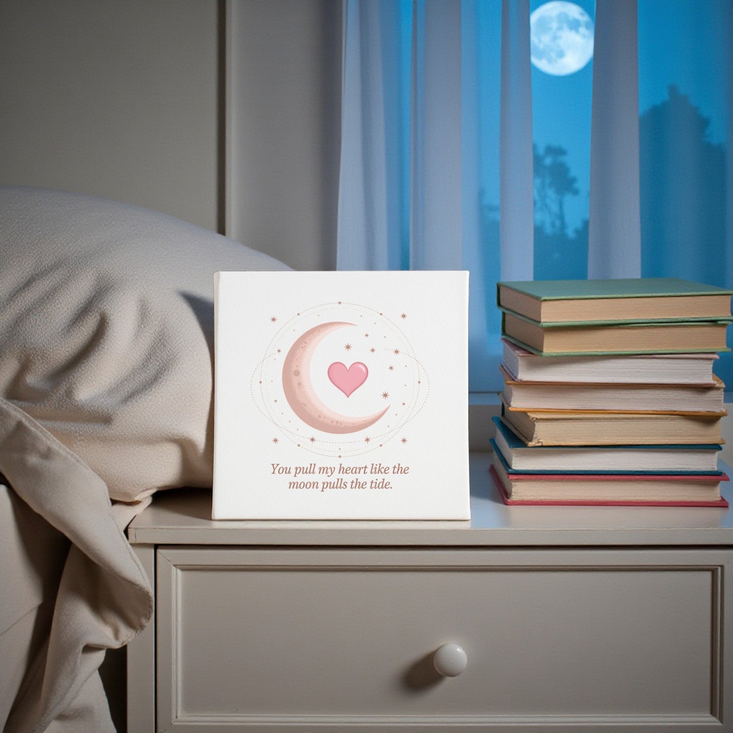 The "Moon Pulls the Tide Love Quote Canvas" by Mirabilia Boutique rests on a bedside table with stacked books, while a full moon glows through the window—adding a romantic, celestial touch to your home decor.