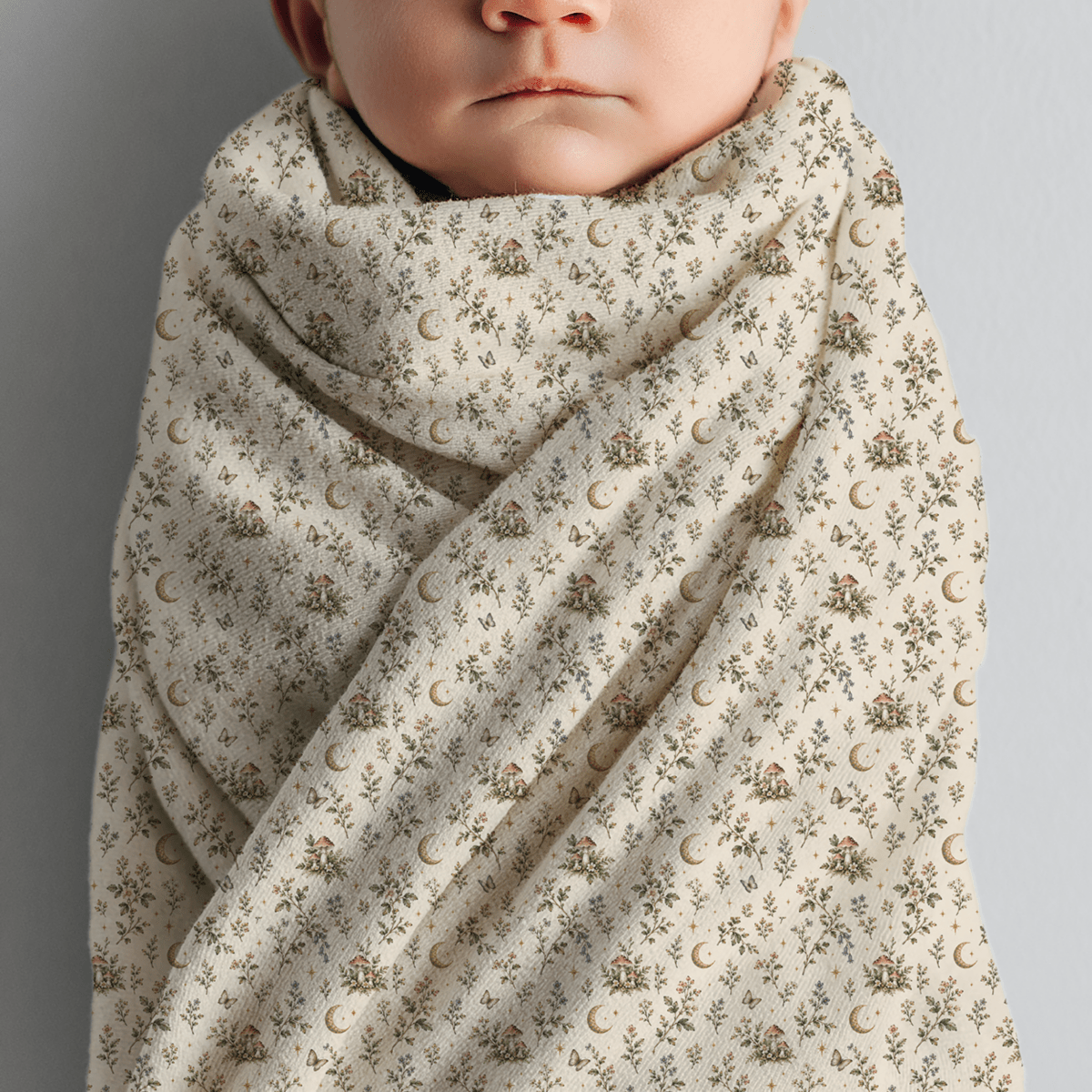 Wrapped in the Moonlit Sprigs Swaddle Blanket from Mirabilia Boutique, featuring a cream-colored botanical design with floral and crescent moon patterns, a baby faces forward against a neutral background—capturing the serene ambiance of a Moon & Moss Nursery.