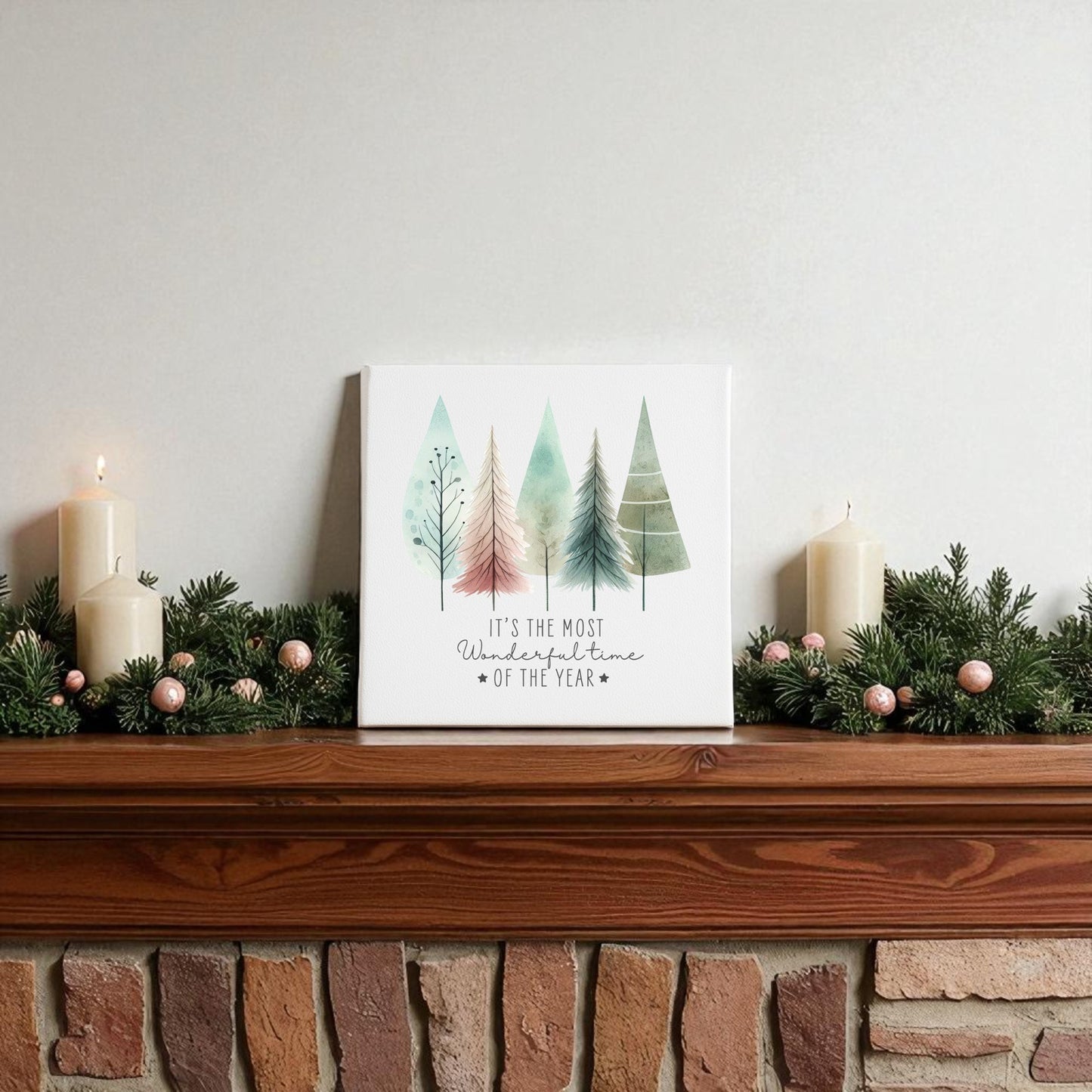 A mantel adorned with pine garland, pink ornaments, candles, and the “Most Wonderful Time of Year Canvas | Pastel Watercolor Trees” by Mirabilia Boutique creates charming winter decor.