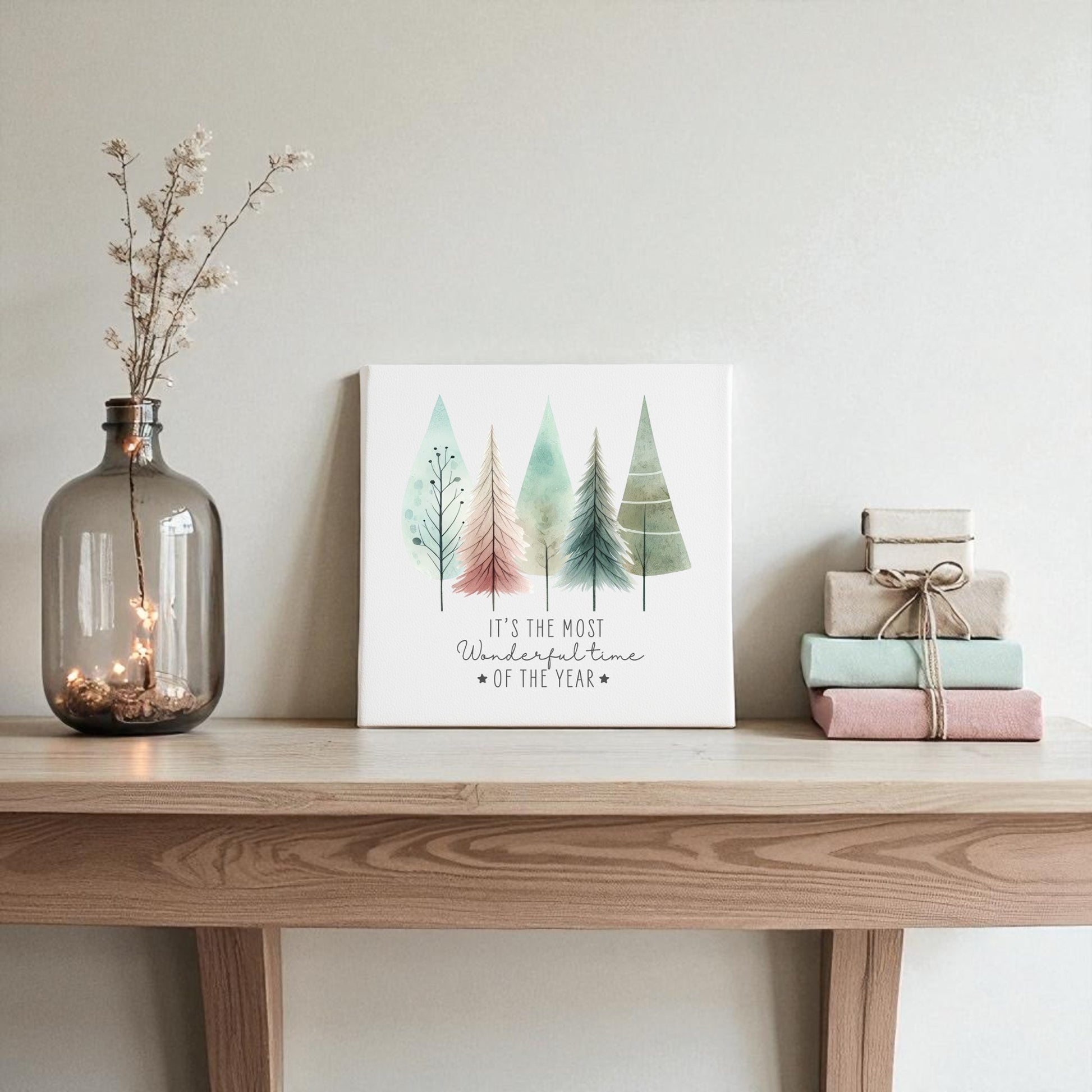 A table featuring the Most Wonderful Time of Year Canvas with pastel watercolor trees by Mirabilia Boutique and a vase of books creates charming winter decor.