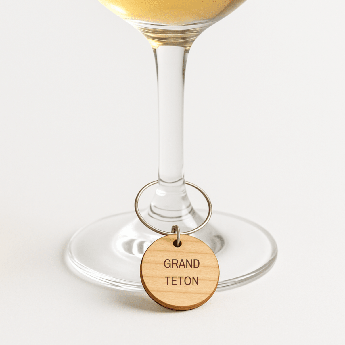 A wine glass features a Mirabilia Boutique Mountain Majesty National Park wine charm labeled "GRAND TETON" around the stem, shown on a plain white background.