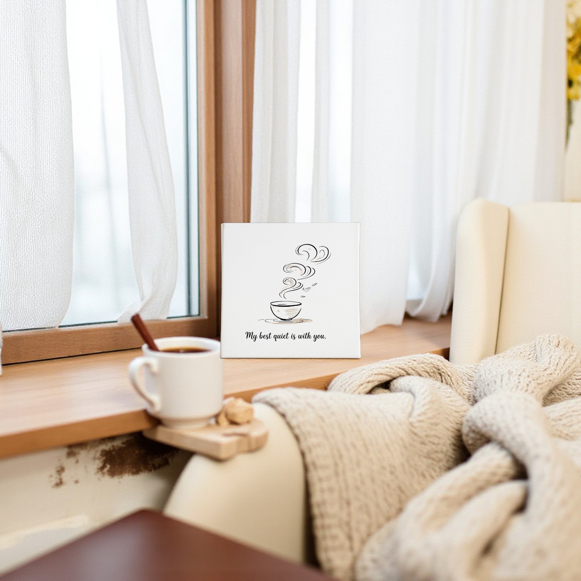 Beside a window sits a cozy chair with a knitted blanket. On the sill rests coffee and Mirabilia Boutique’s Best Quiet Canvas—minimalist wall art with a coffee cup and the quote, "My best quiet is with you." A heartfelt gift.