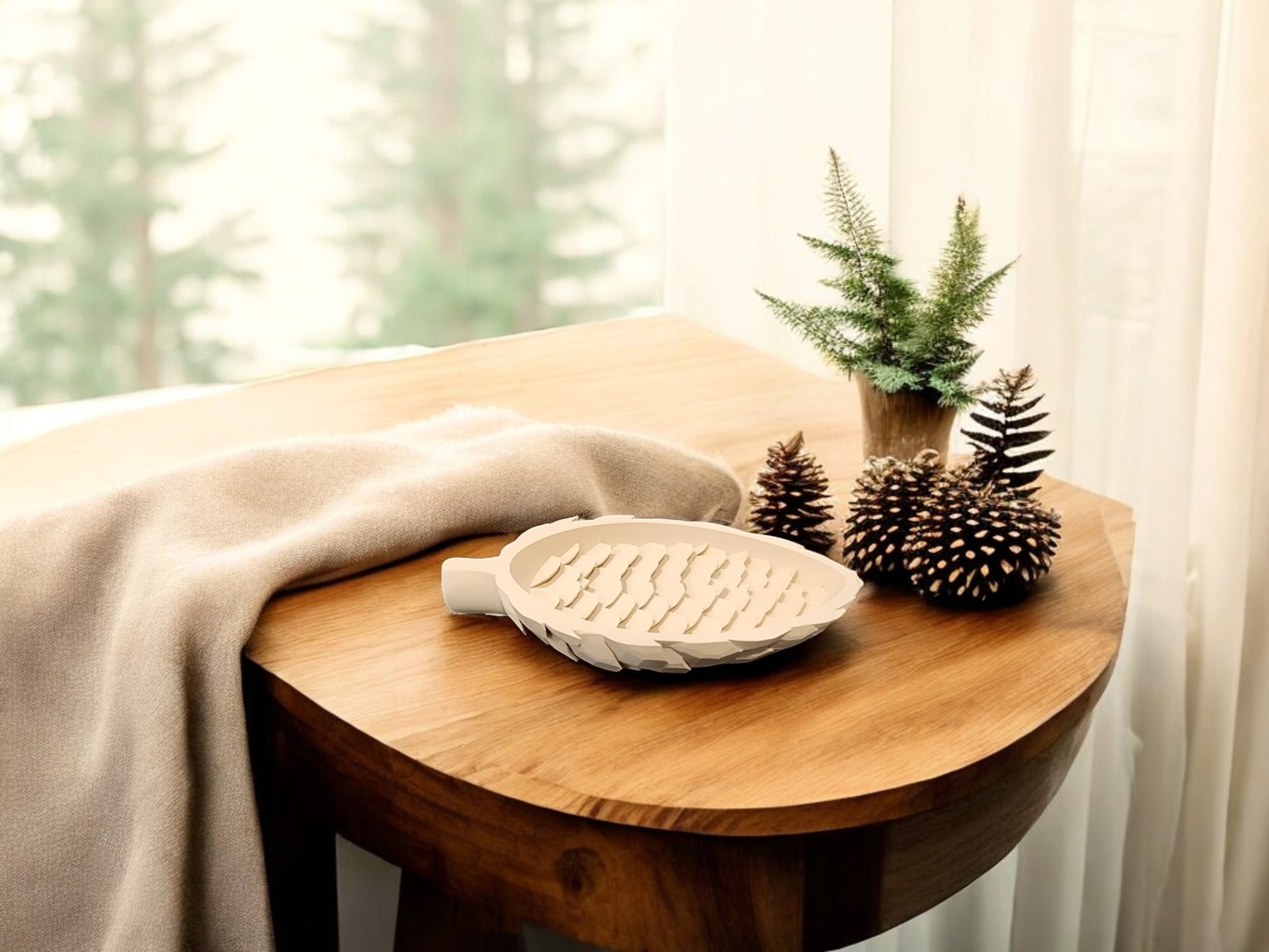 A wooden table by a window features Mirabilia Boutique’s Light Brown Pinecone Tray for Spring & Fall Decor, a potted plant, and a beige blanket. Sunlight filters through sheer curtains, enhancing the natural woodland charm.
