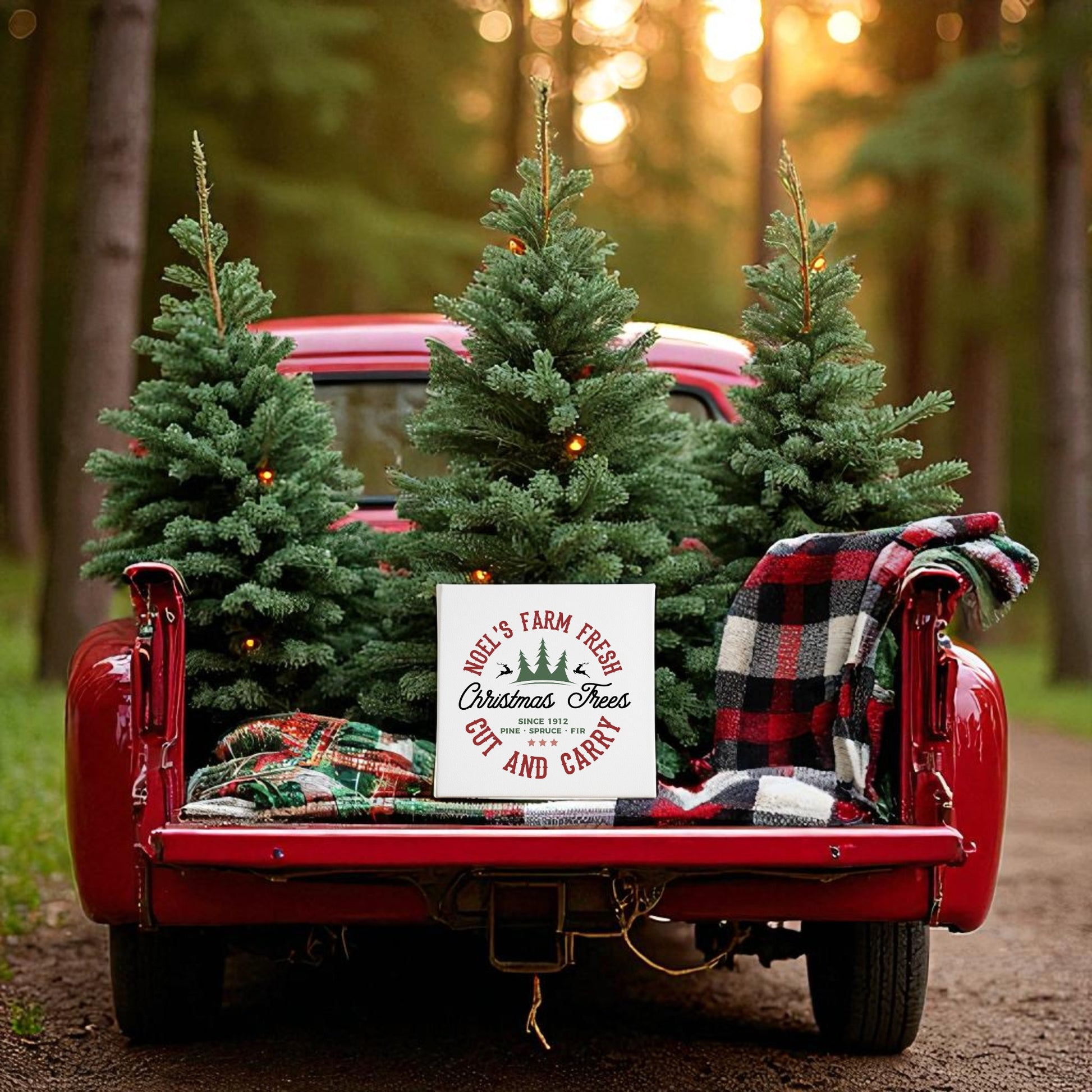 A red vintage truck with plaid blankets and Christmas trees is parked at sunset in a forest. A Mirabilia Boutique Farm Fresh Christmas Tree Sign, Rustic Holiday 8x8 Canvas, decorates the scene for festive charm.